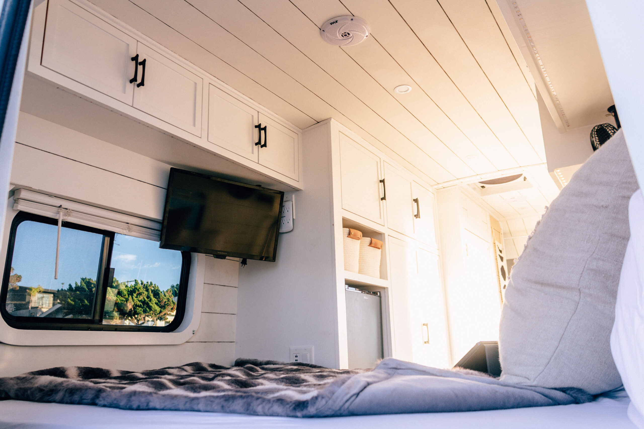 This bright RV rental interior features a cozy bed, wall-mounted TV, white cabinets, and a scenic window view.. Ford Custom Transit 2019