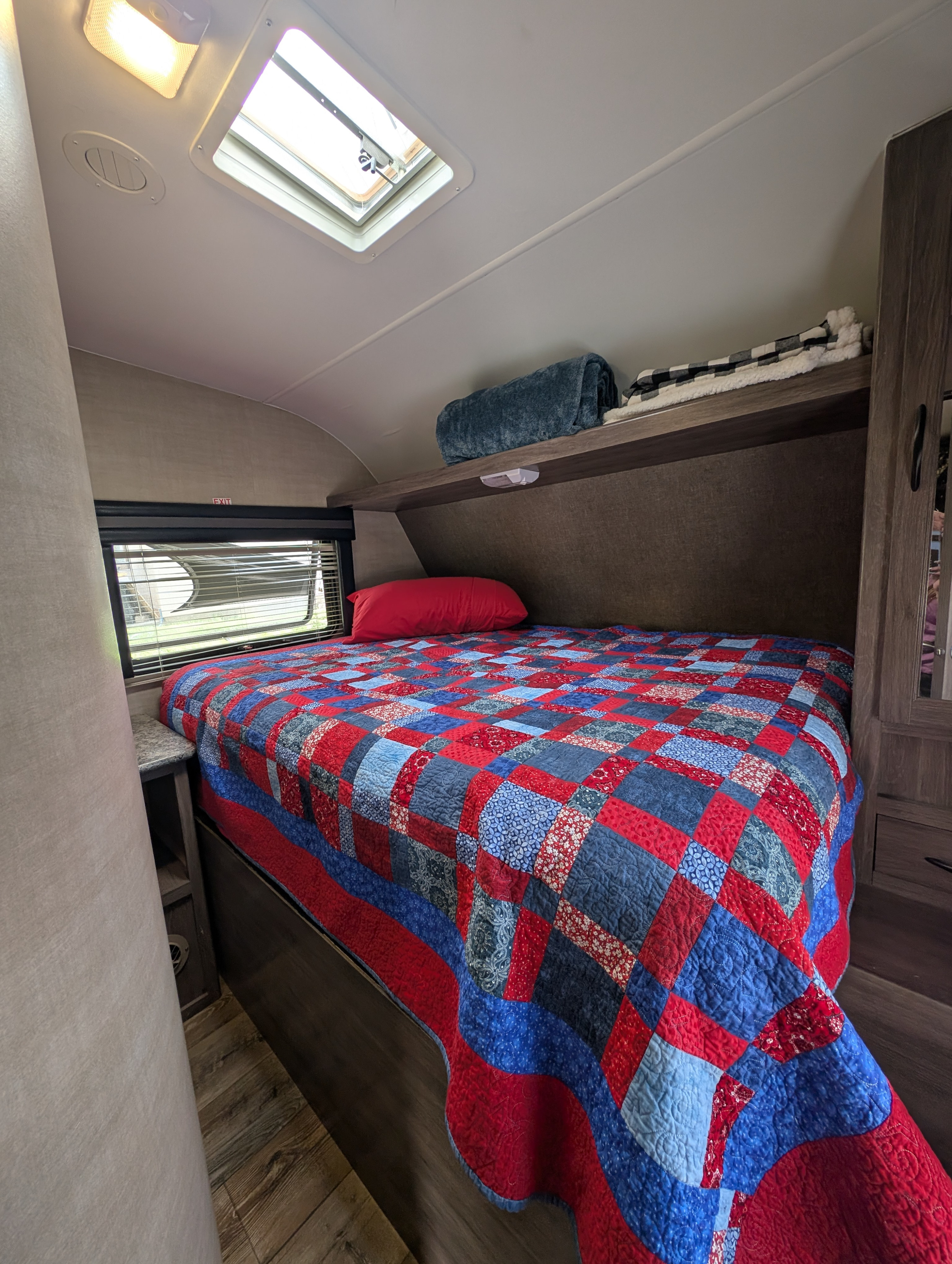 Cozy RV rental bedroom featuring a colorful patchwork quilt, overhead storage, a bright skylight, and window.. Pacific Coachworks Powerlite 2018