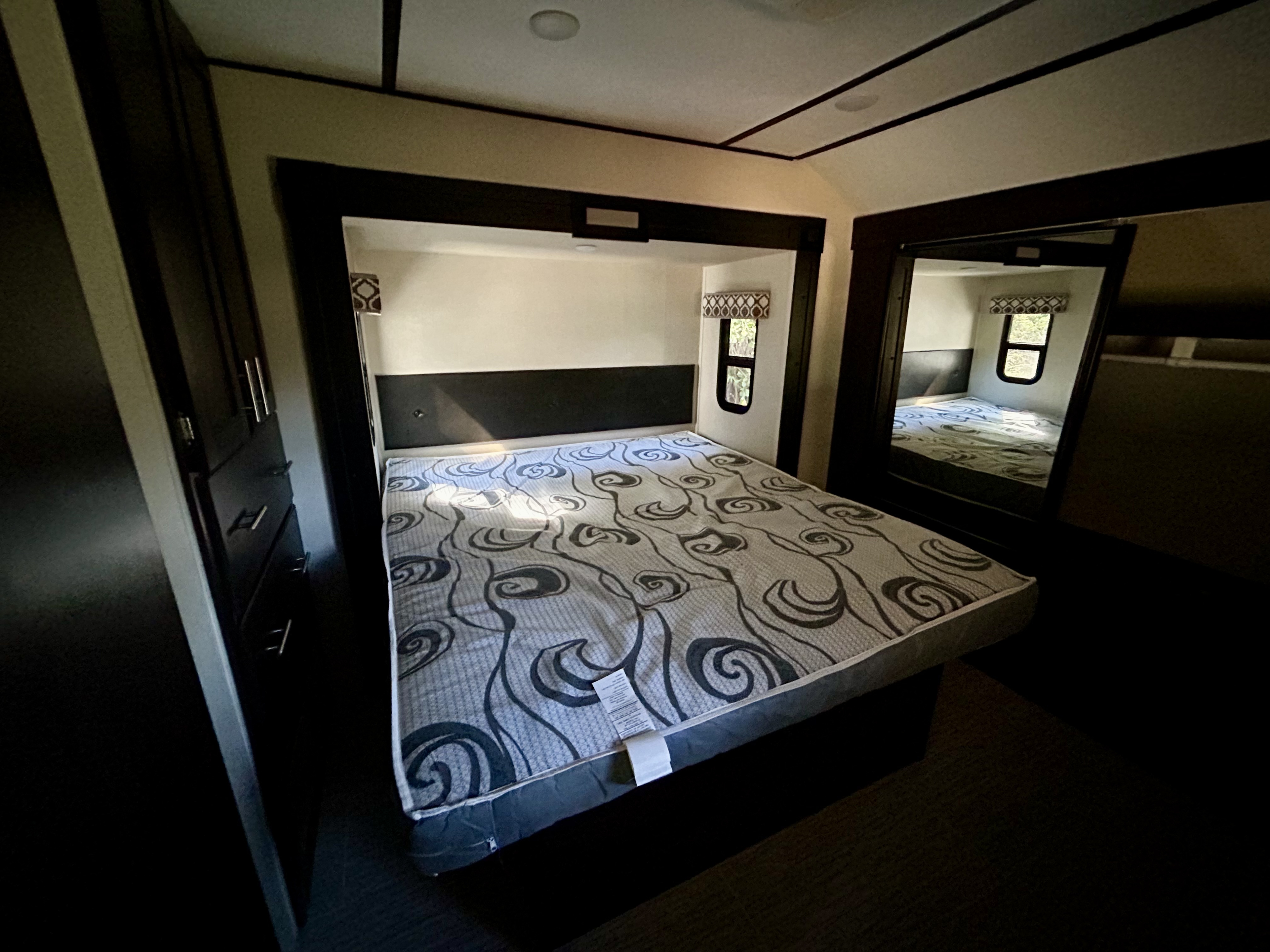 Spacious RV rental bedroom featuring a bed with a grey patterned mattress, dark built-in storage, and a large mirror.. Primetime Lacrosse 2019