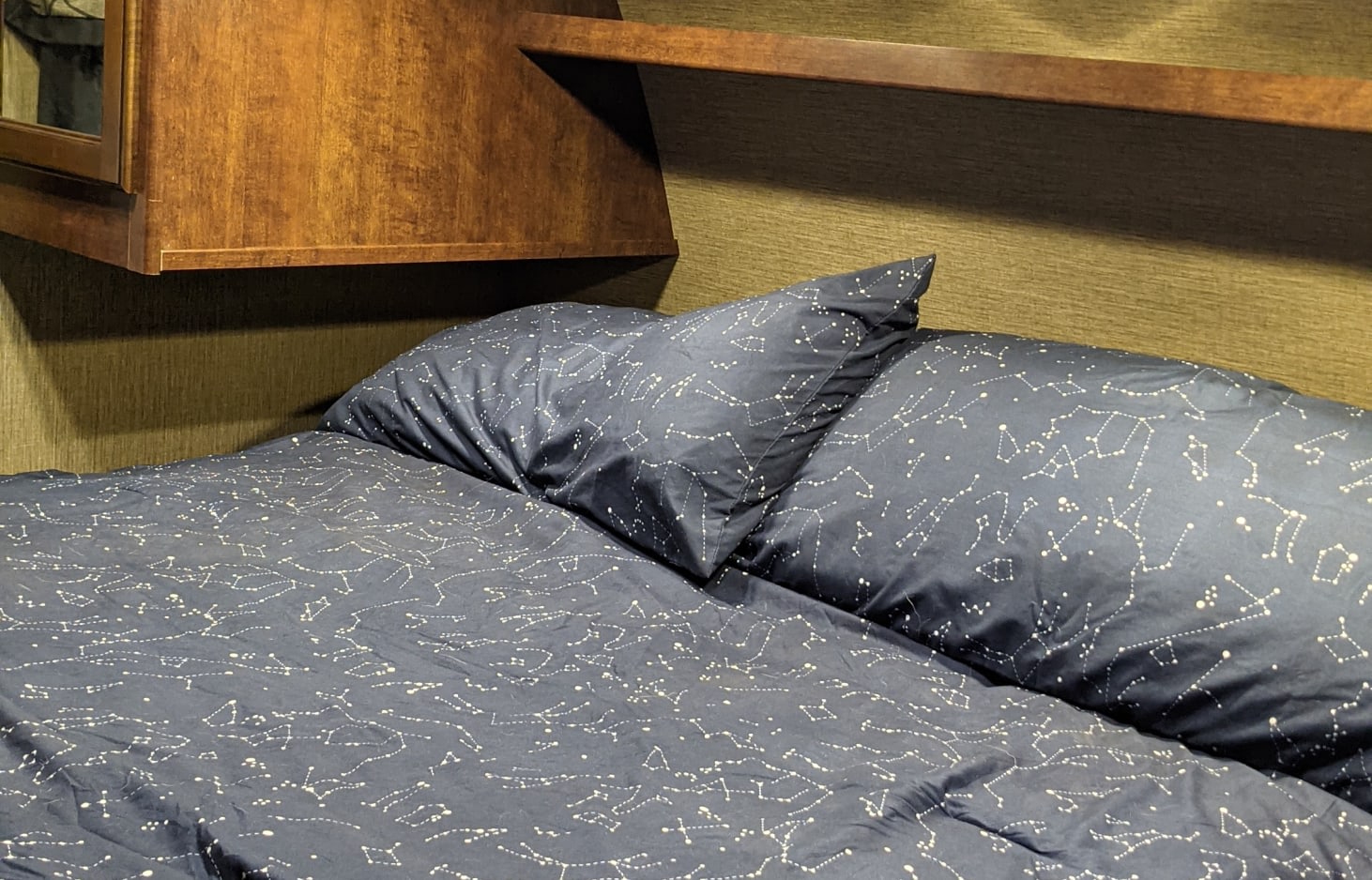 Cozy RV rental bed featuring dark blue constellation bedding and wood cabinets. Perfect for a comfortable night's rest.. Keystone RV Outback Ultra-Lite 2016