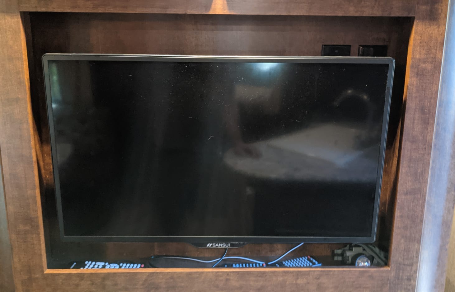 RV rental entertainment: Sansui TV within a dark wood cabinet, with power outlets and cables below.. Keystone RV Outback Ultra-Lite 2016