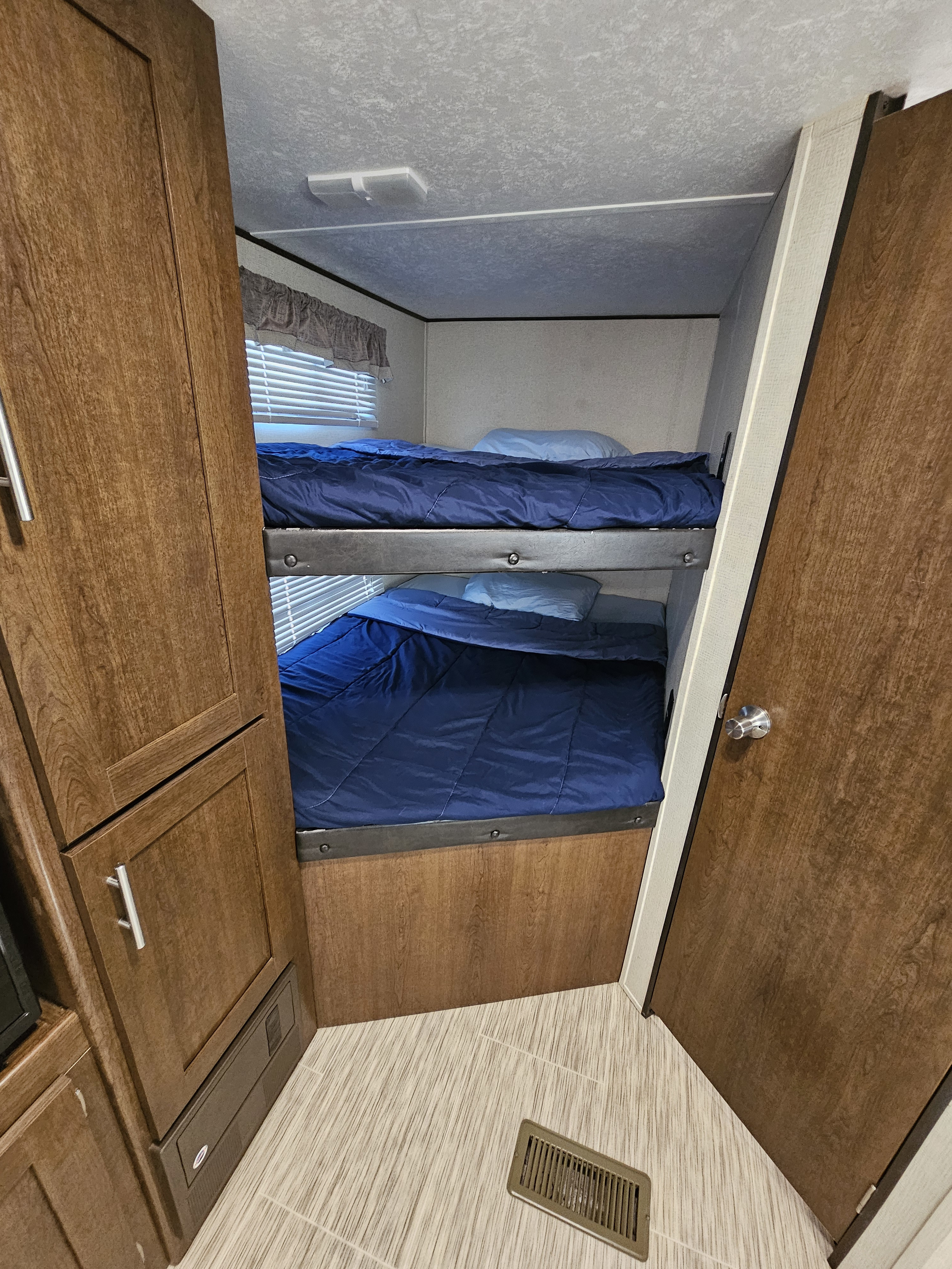 RV rental sleeping area: two bunk beds with blue comforters, wooden cabinets, and a window. Perfect for travelers.. Avenger ATI 2019