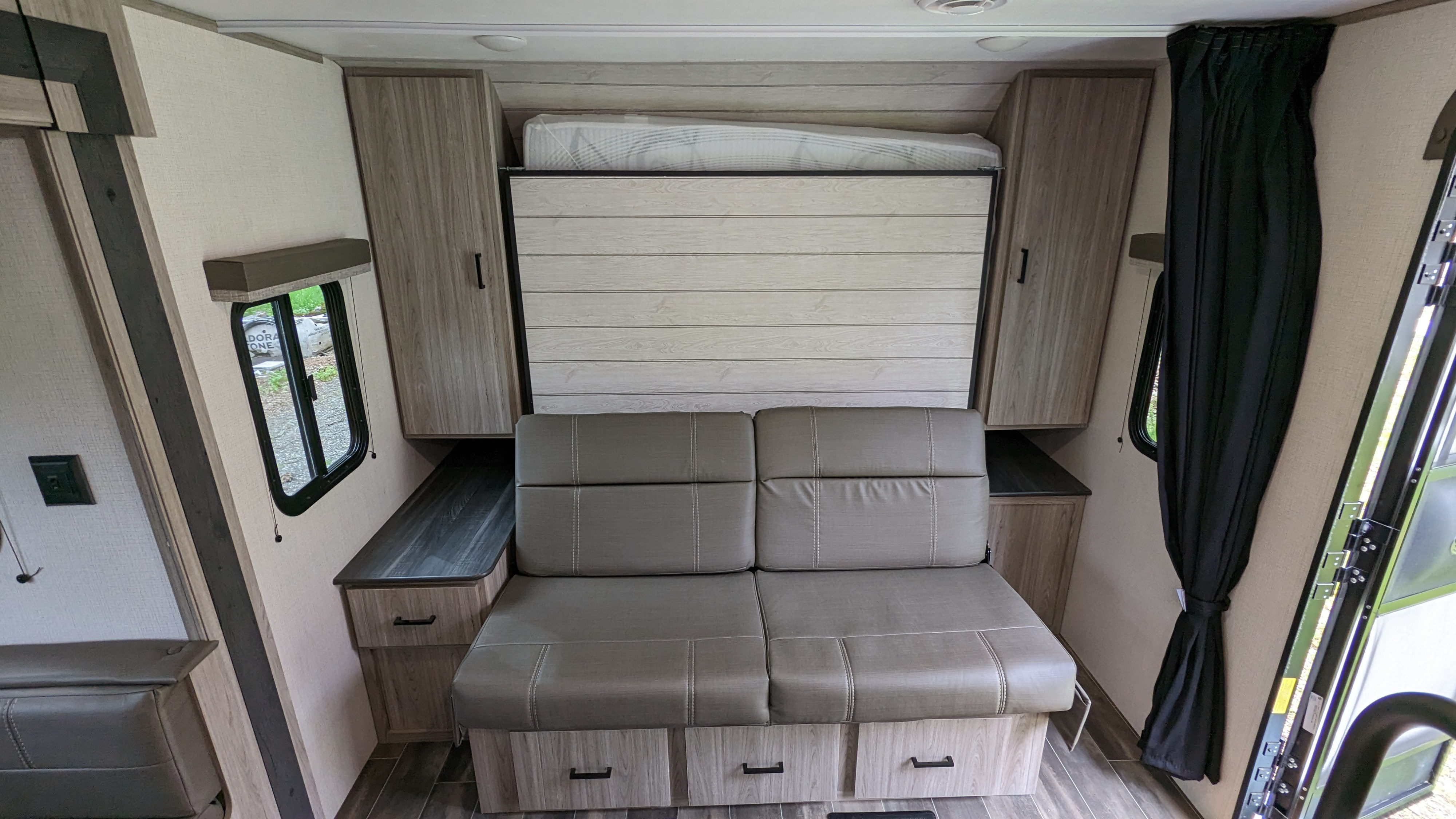 RV rental interior: a gray sofa with under-storage and a hidden wall-mounted Murphy bed, flanked by wood-look cabinets.. Keystone RV Passport SL 2022