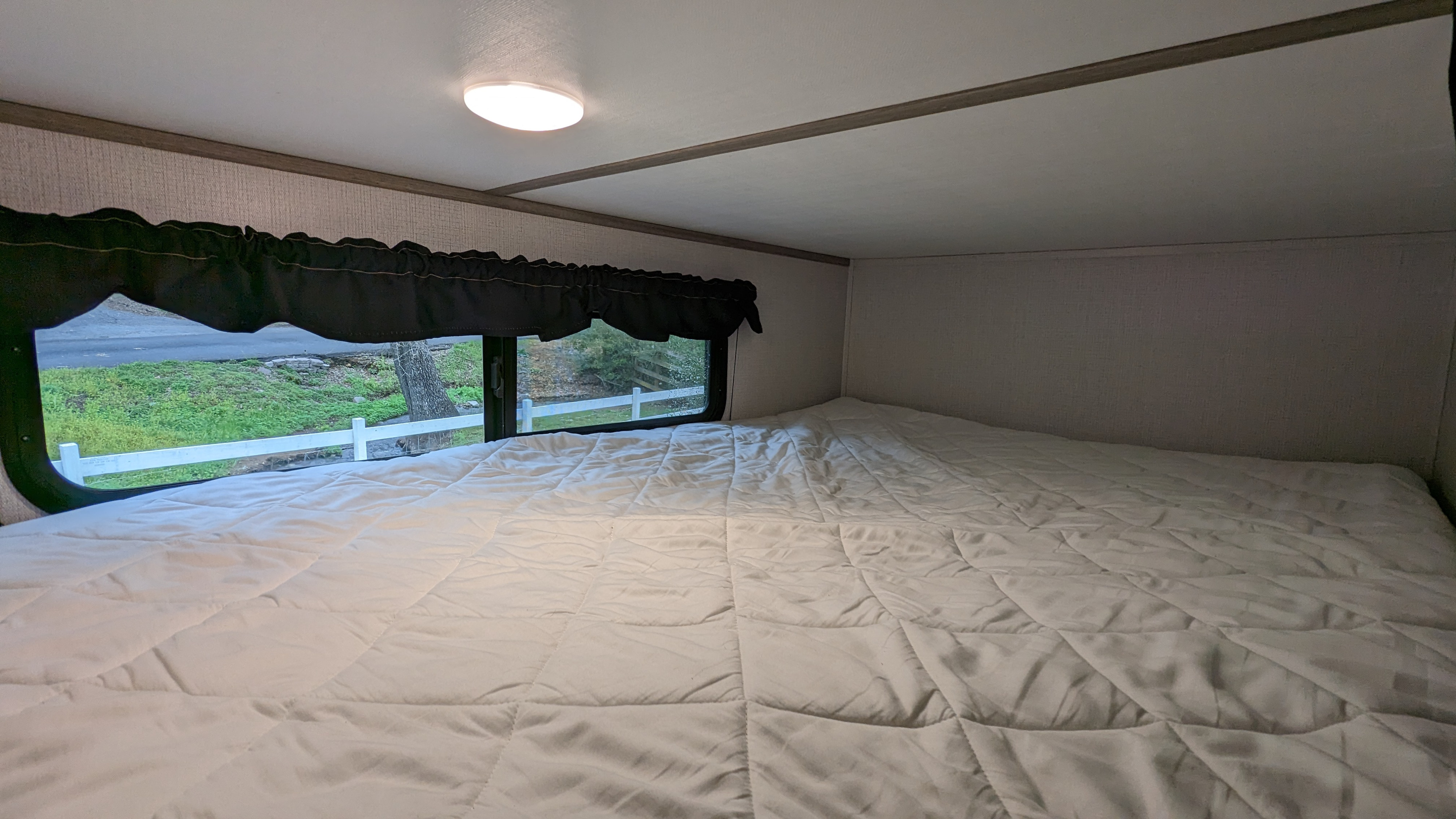Cozy RV rental bedroom featuring a comfy white bed, ceiling light, and a window offering a scenic view of nature.. Keystone RV Passport SL 2022