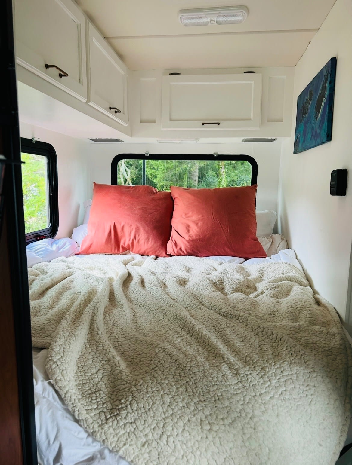 Cozy RV rental bedroom features a comfy bed, coral pillows, sherpa blanket, and scenic nature views from the windows.. Thor Chateau 2016