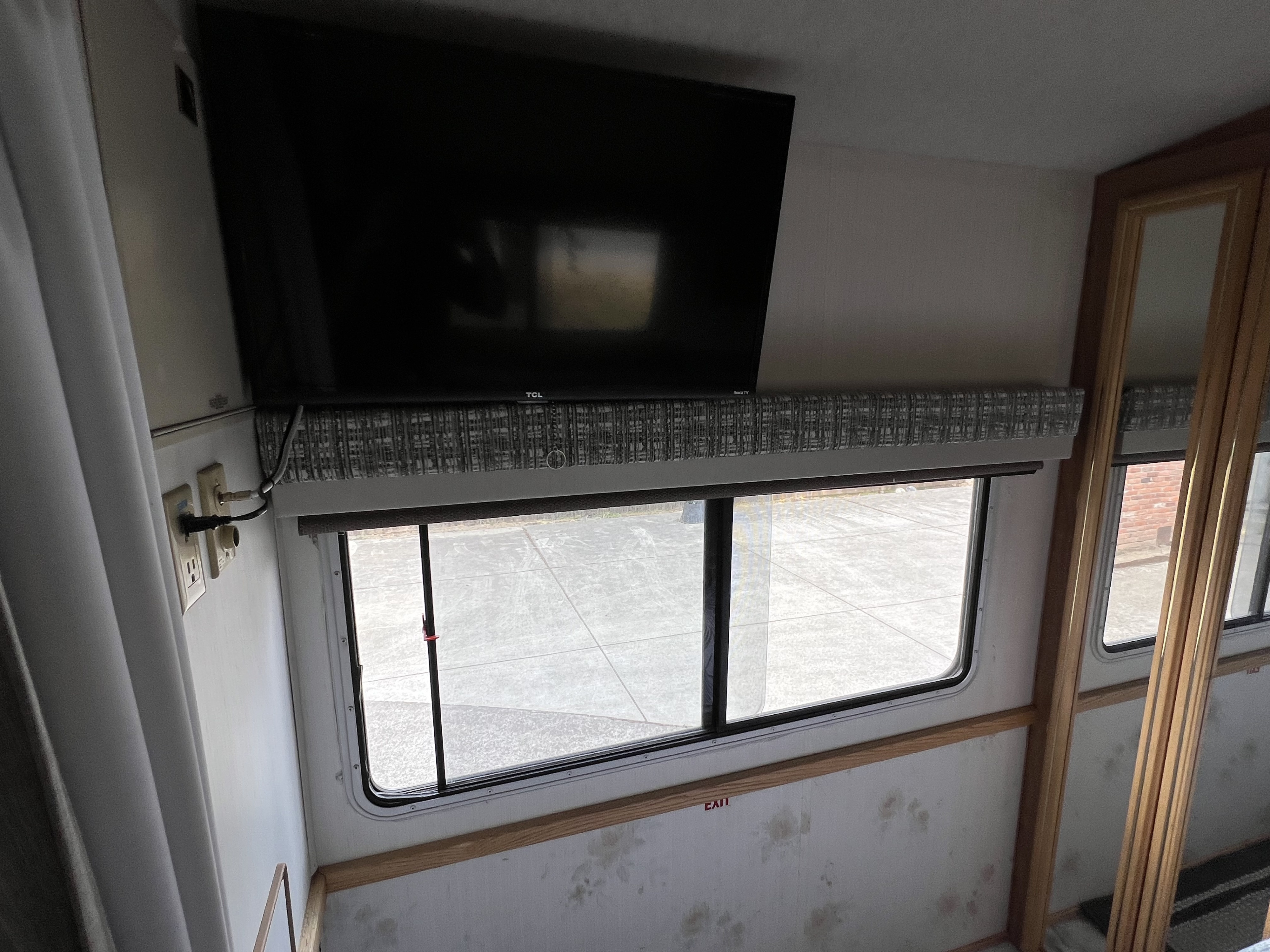 RV rental interior: mounted TV above window, patterned valance, outlets, and wooden trim.. Fleetwood Tioga Sl 1998