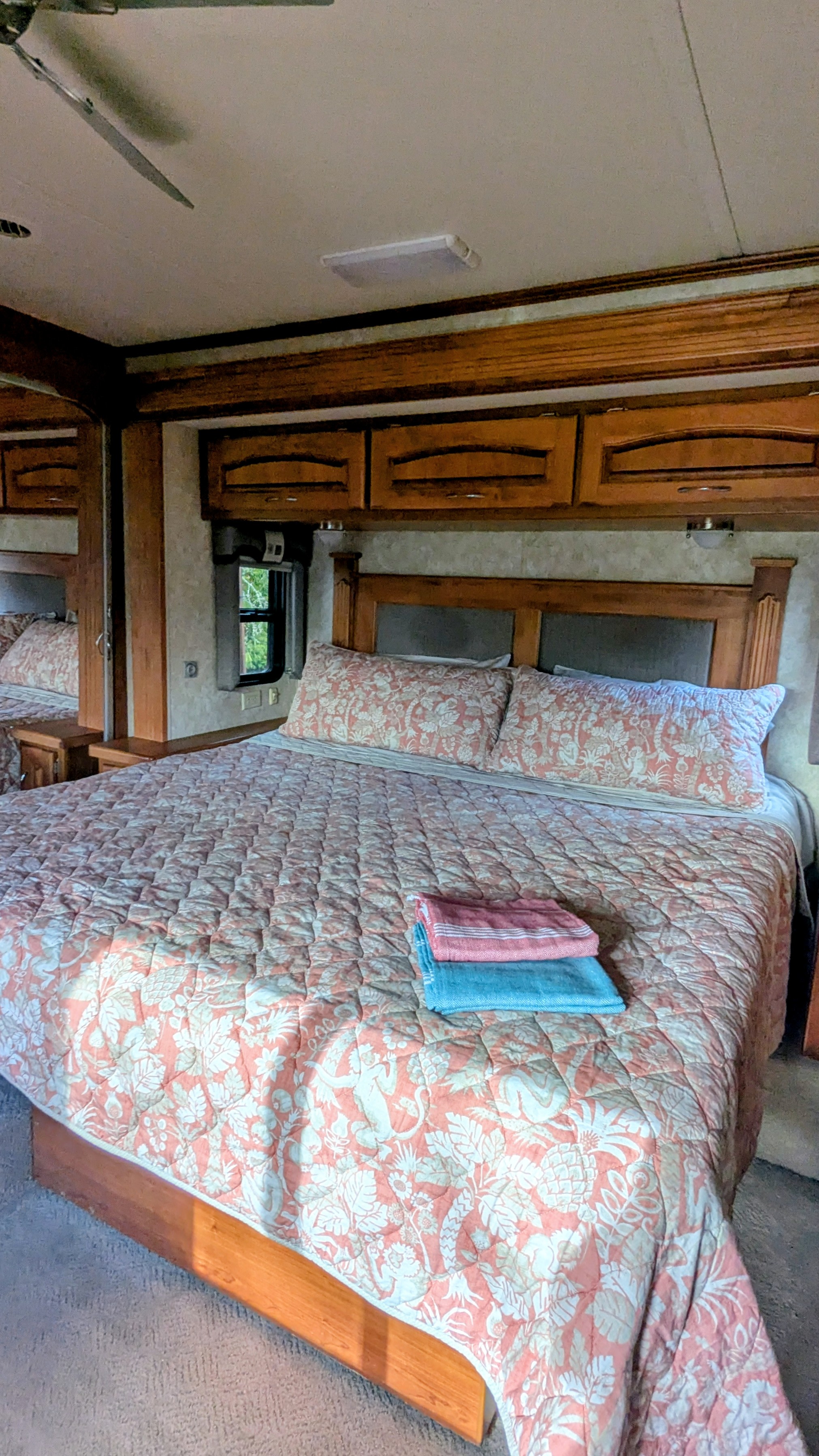 Cozy RV rental bedroom with patterned bedspread, wooden cabinets, and ceiling fan. Perfect for your next adventure.. Holiday Rambler Ambassador 2007