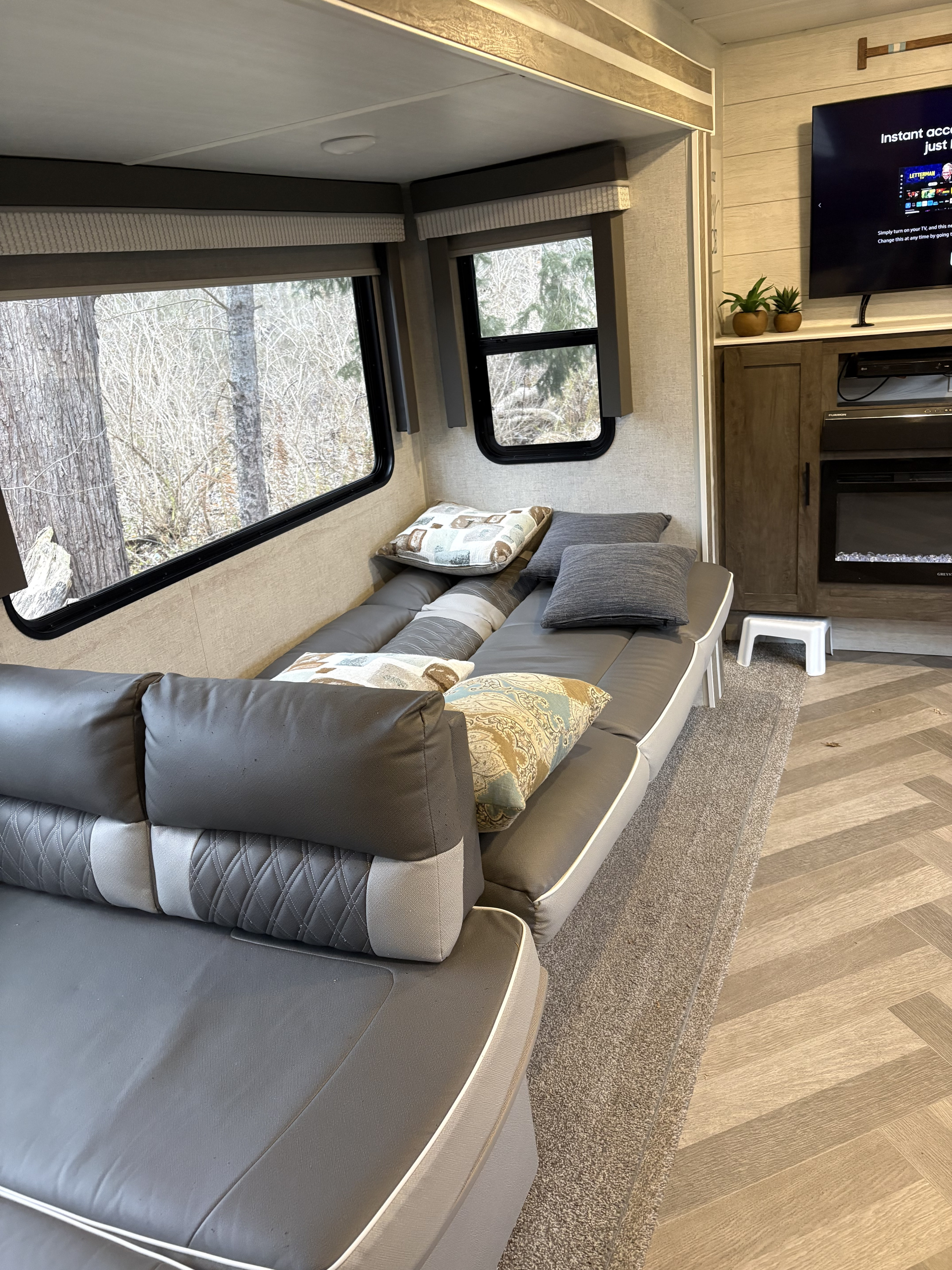 Cozy rv rental living area featuring a gray sofa, large windows with outdoor views, and a TV above a fireplace.. Forest River Salem 2021