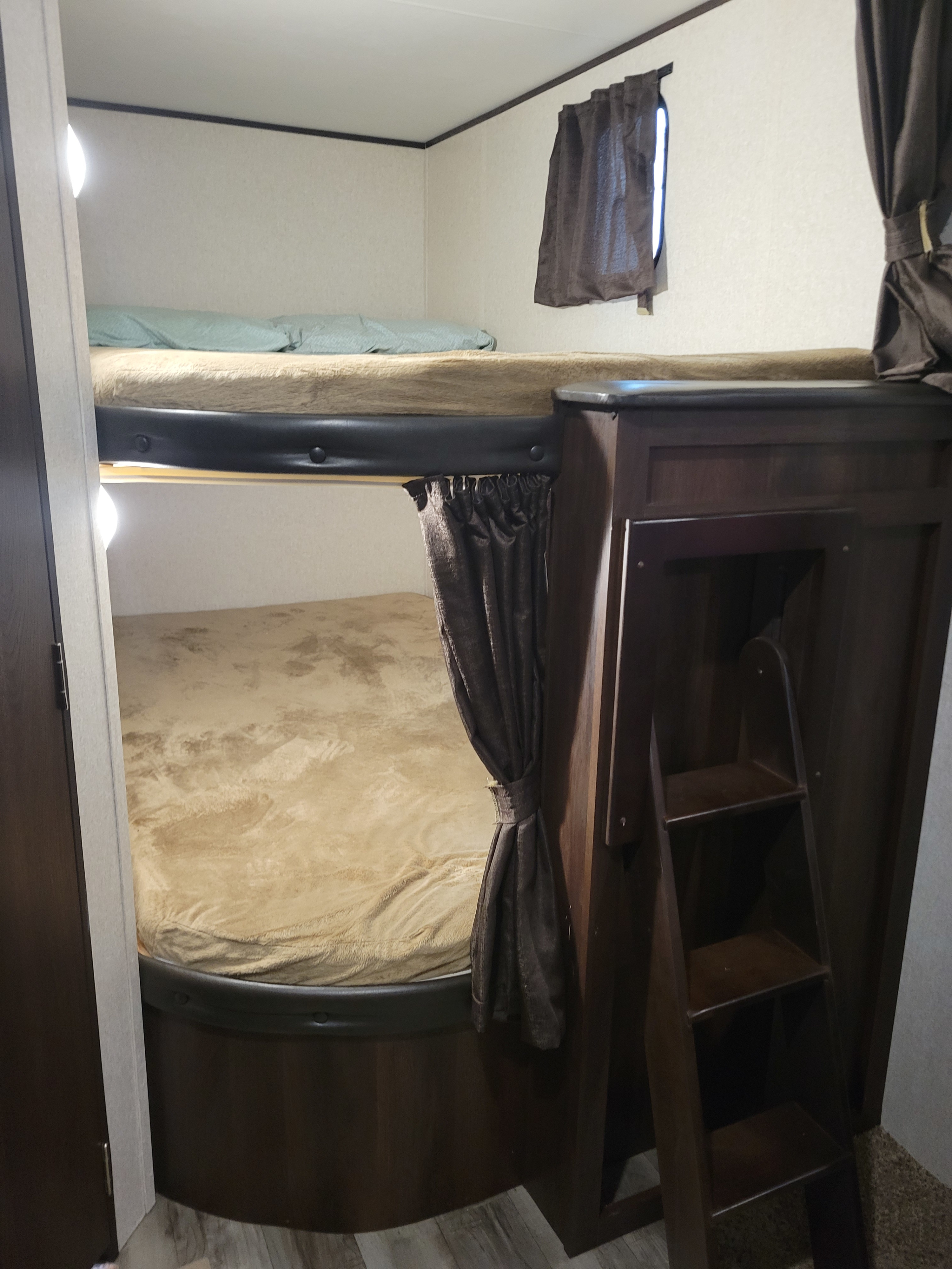 Cozy RV rental interior featuring dark wood bunk beds, a ladder, curtains, and light-colored bedding in a compact space.. Jayco Jay Flight 2018