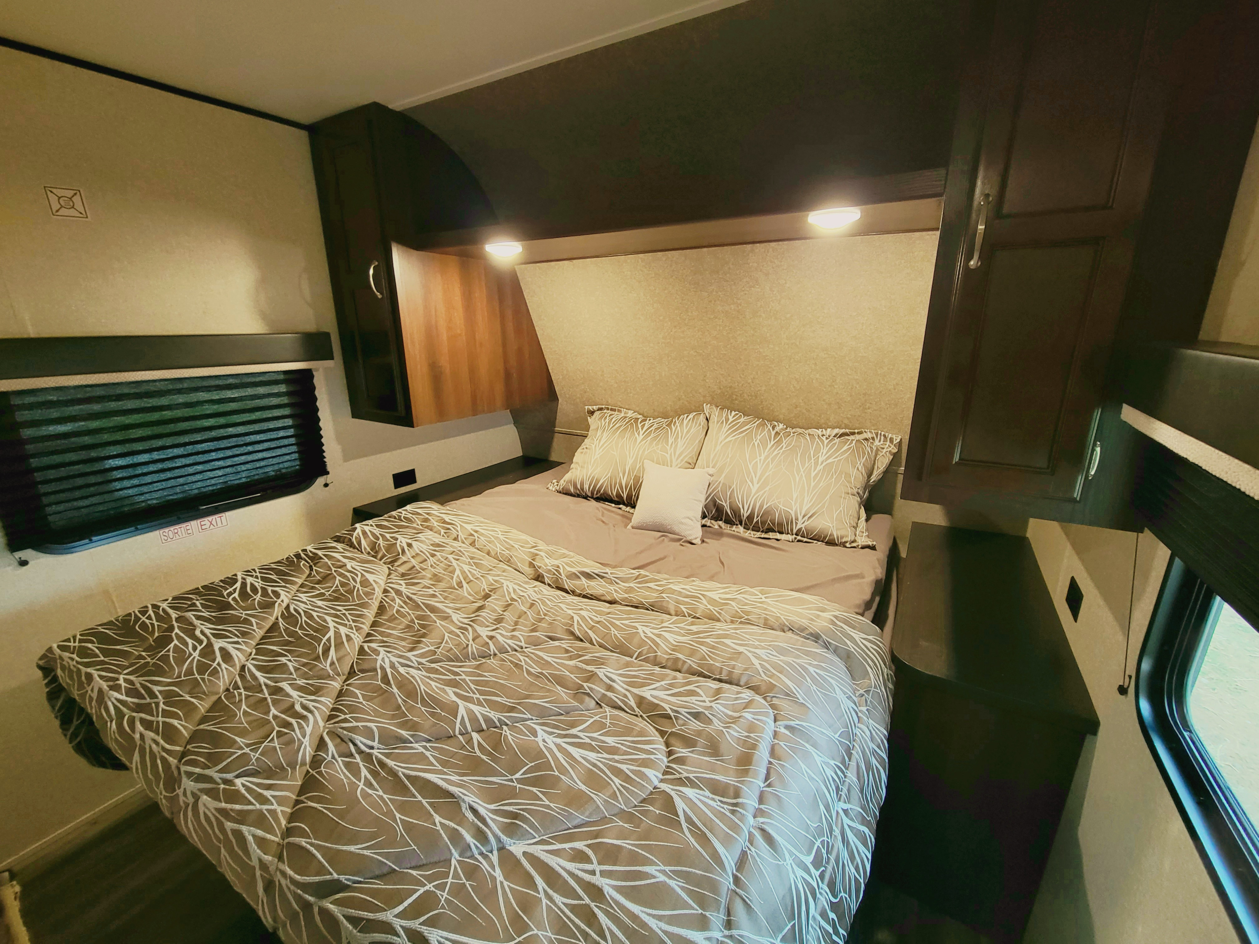 Cozy RV rental bedroom with patterned bedding, overhead cabinets, and an emergency exit window, ideal for travel.. Jayco Jay Flight 2018
