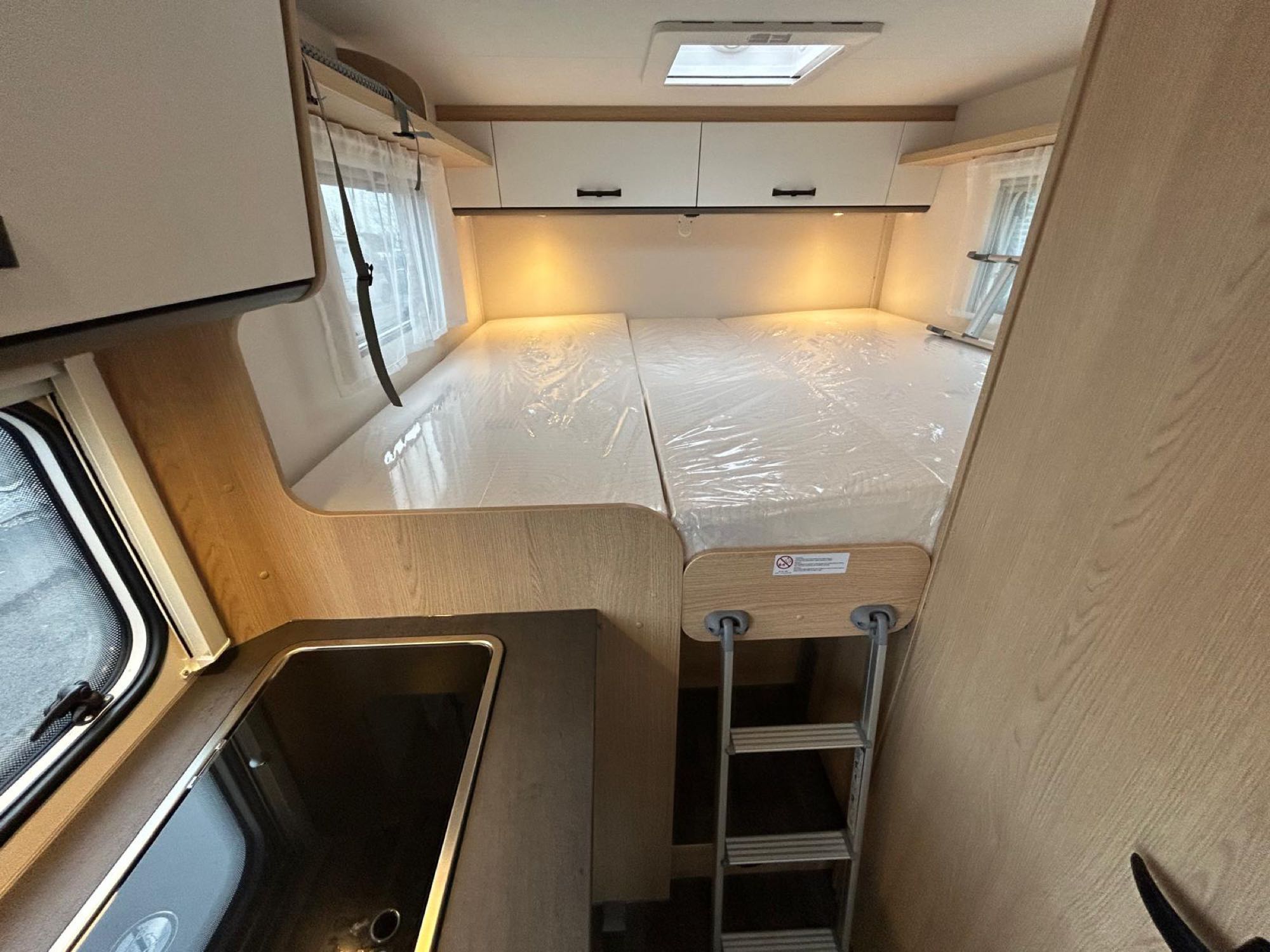 Clean rv rental interior showing a bed with ladder, overhead storage, and a compact kitchenette on the left.. Sunlight V67S 2026