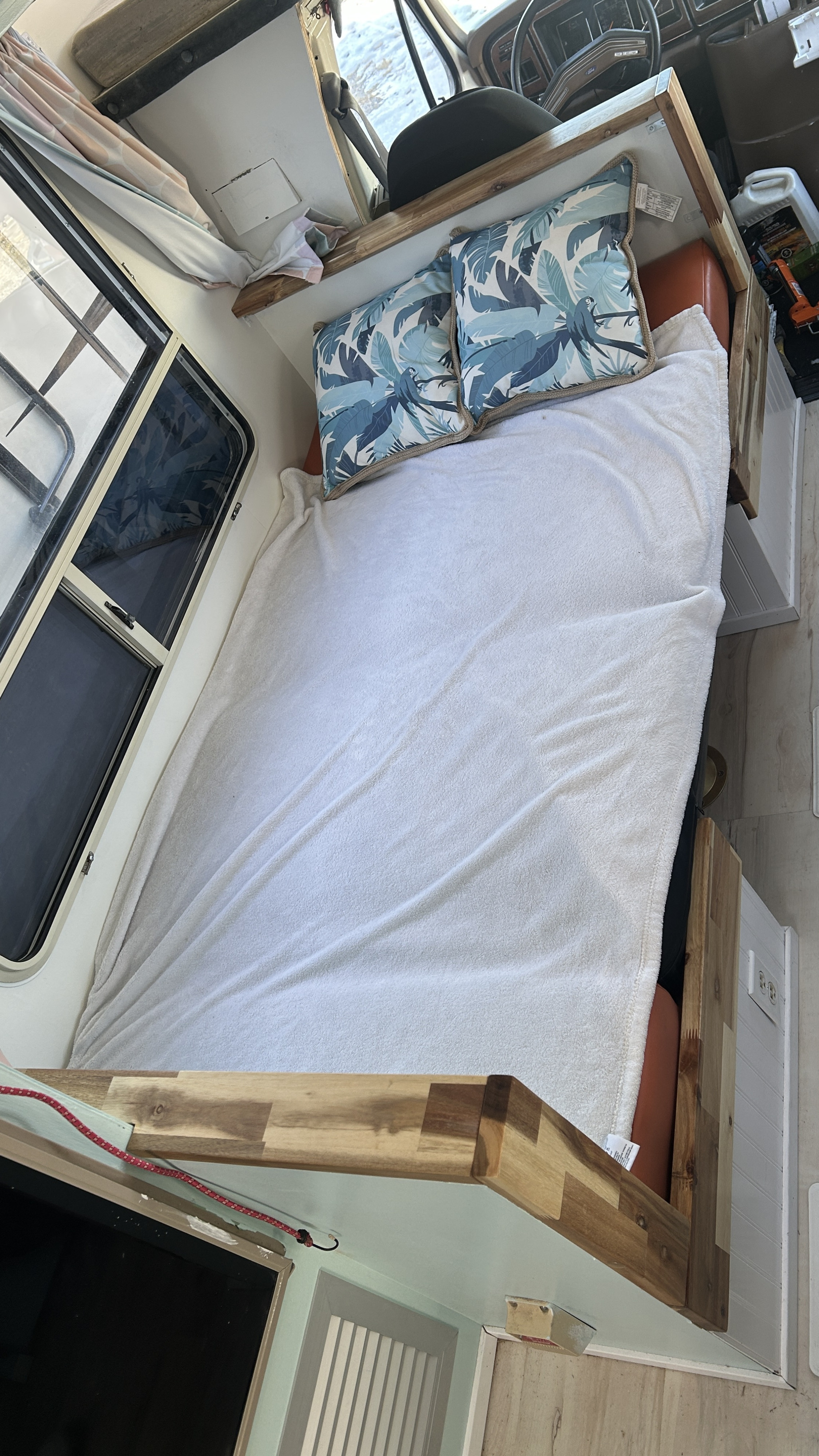 Cozy bed in an RV rental, featuring tropical pillows, a white blanket, and windows in the camper's interior.. Ford Econoline 1988