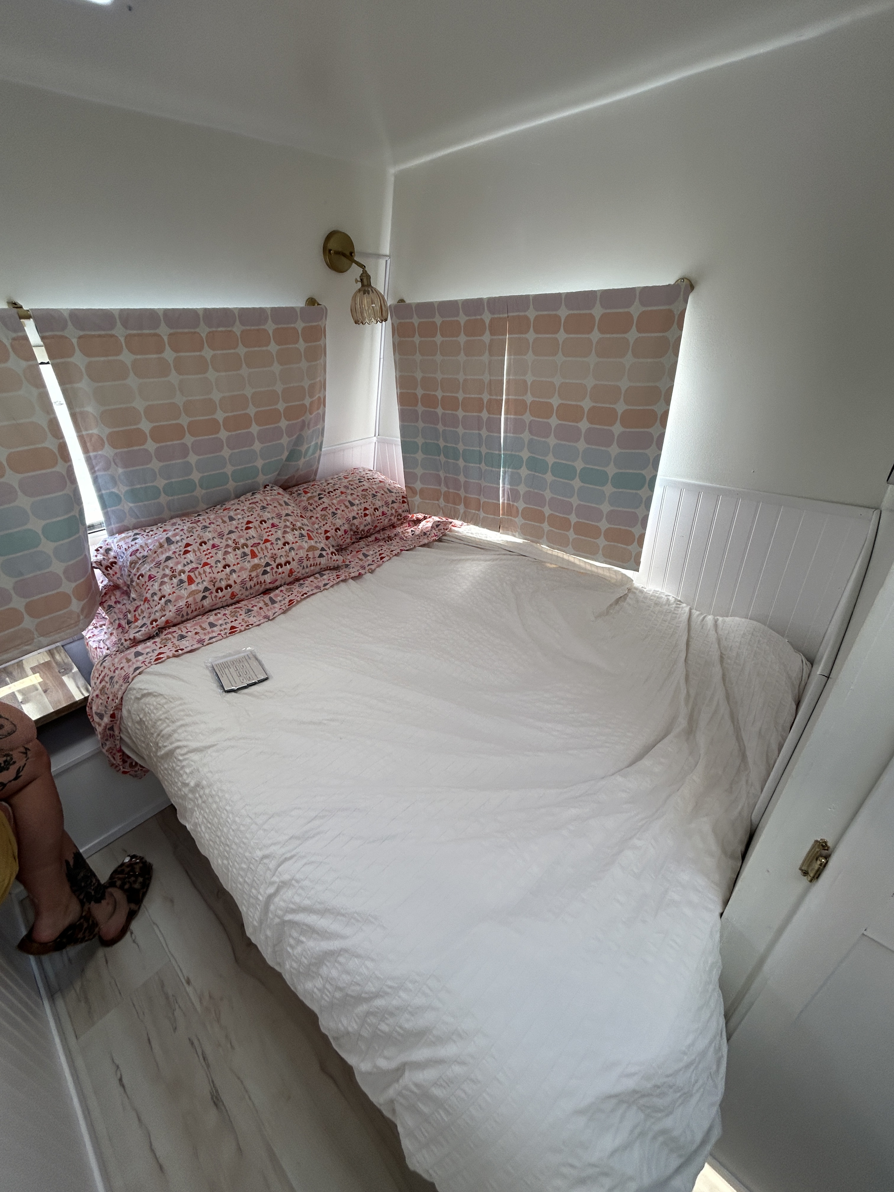 Cozy RV rental bedroom featuring a neatly made bed, cheerful patterned window shades, and a wall-mounted light.. Ford Econoline 1988