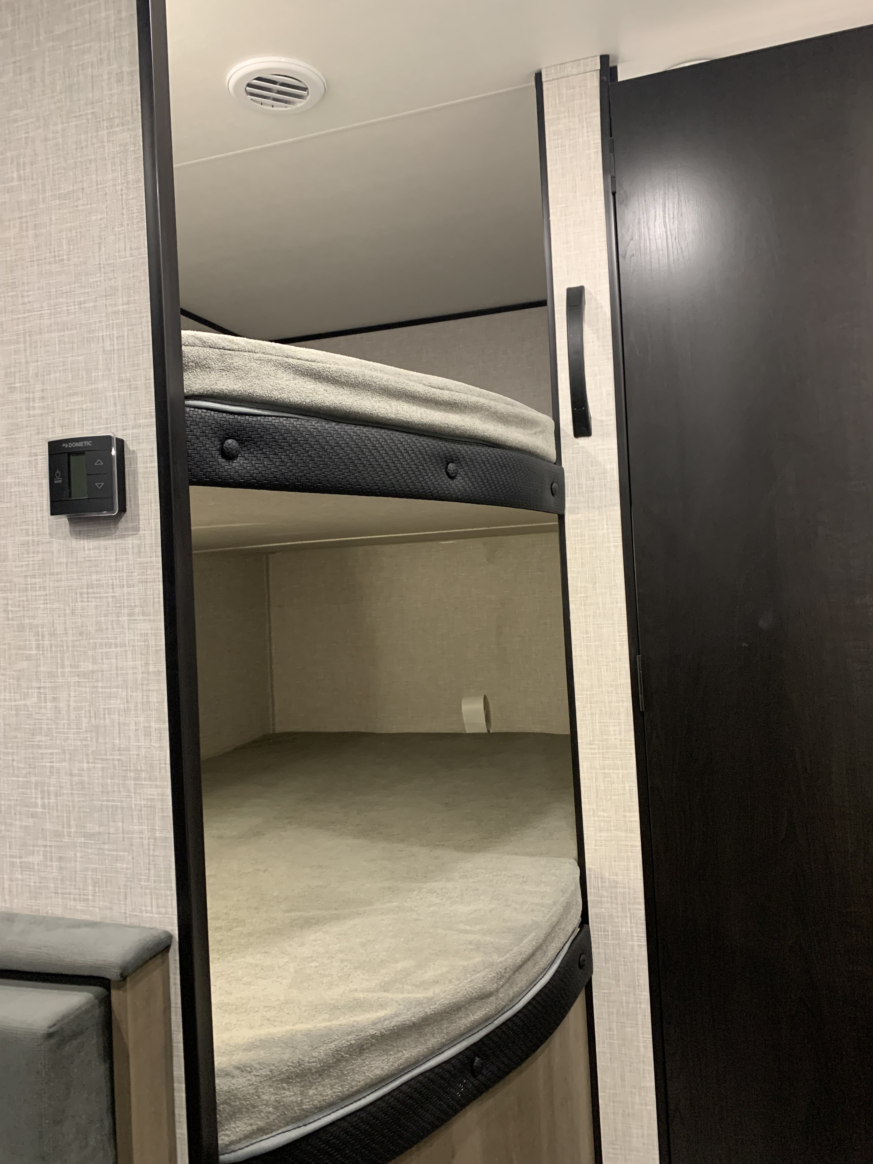 This RV rental interior features two bunk beds with gray mattresses. A Dometic thermostat is on the left wall, and an air vent is on the ceiling.. Jayco Jay Flight SLX 2025