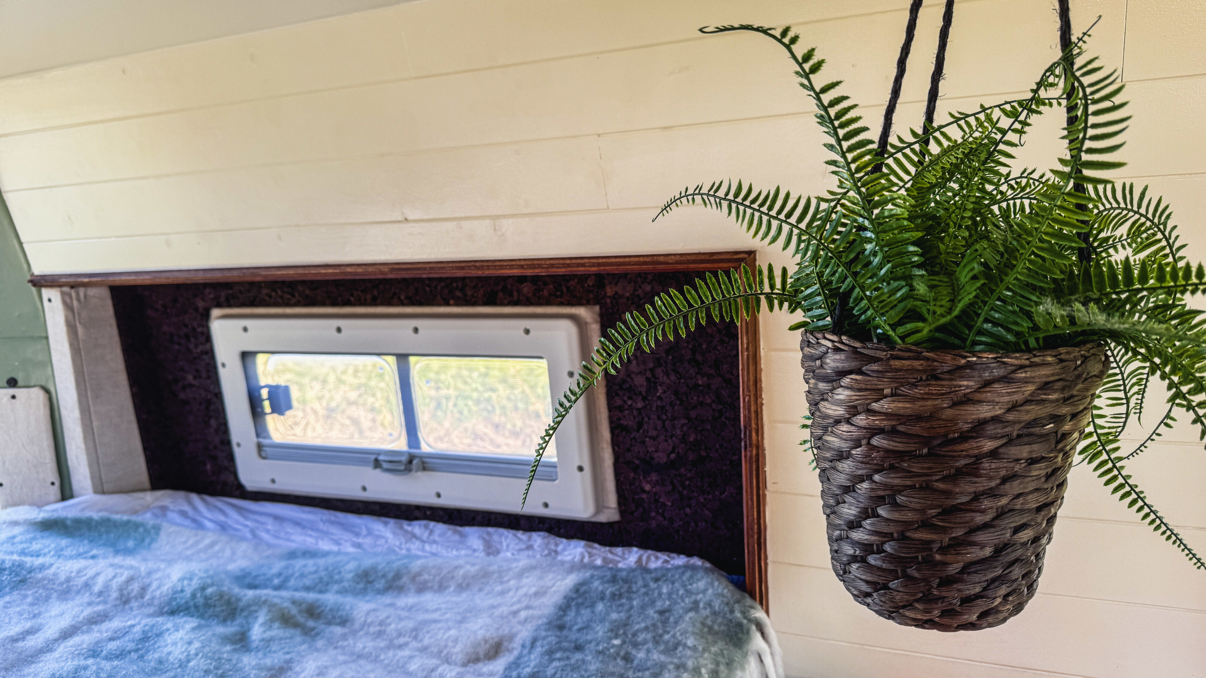 Cozy RV rental bedroom with a light blue blanketed bed, window, and a decorative hanging fern plant.. Opel Movano 2015