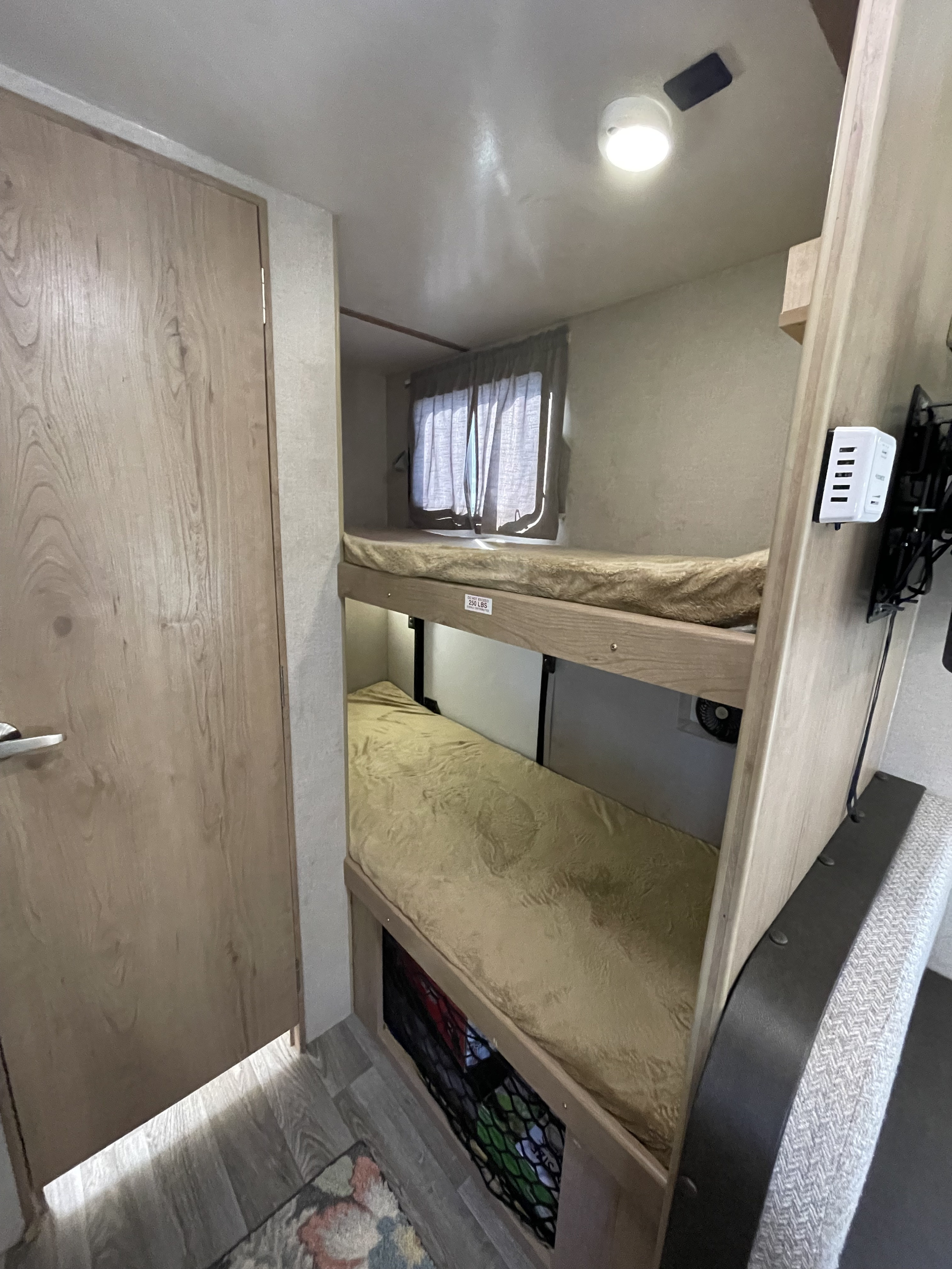 Compact RV rental interior featuring cozy bunk beds with tan mattresses, a window, ceiling light, and charging station.. Winnebago Minnie Winnie 2020