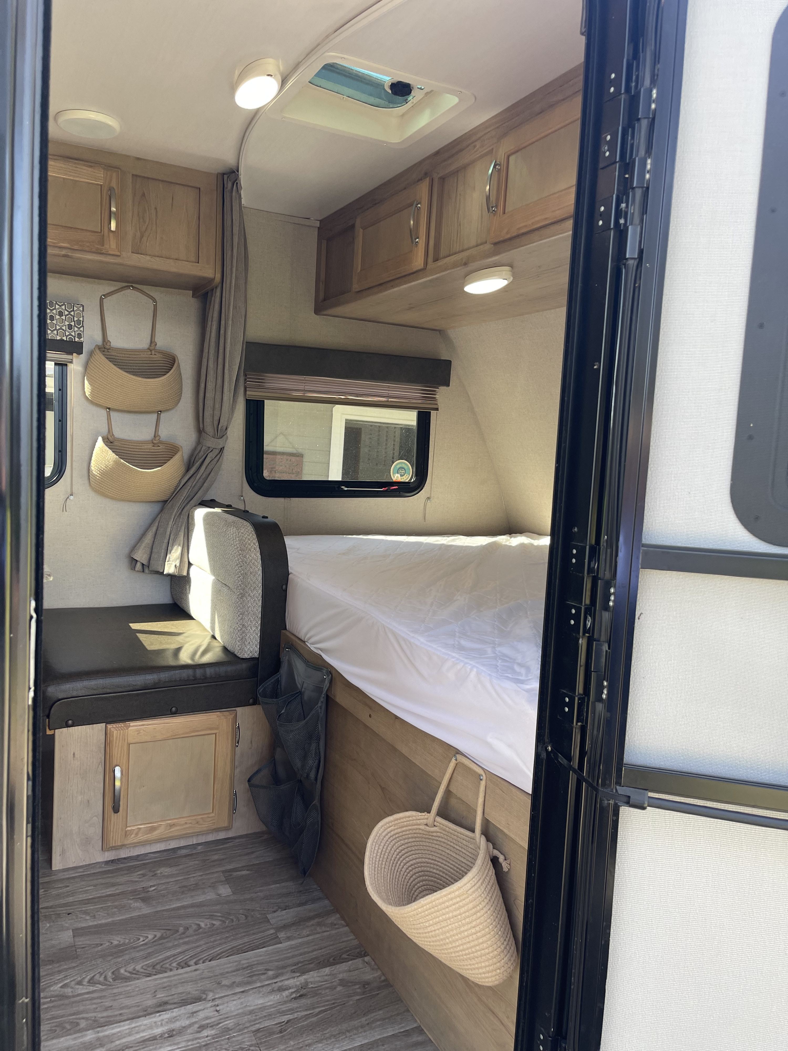 Inside an RV rental, a compact bedroom features a bed, built-in bench seating, overhead cabinets, and hanging storage baskets.. Winnebago Minnie Winnie 2020