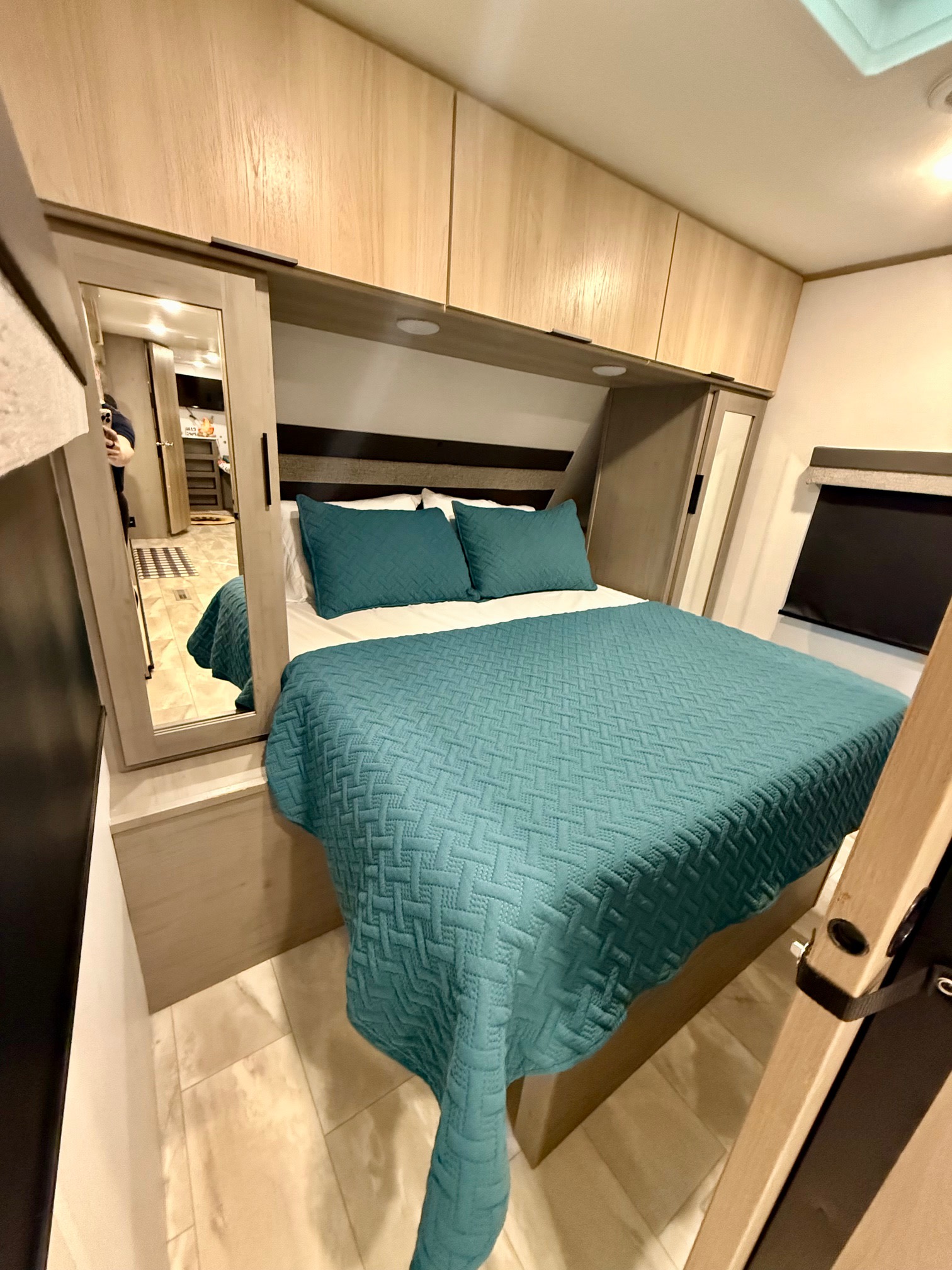 Enjoy this RV rental bedroom: queen bed with quilted teal bedding, light wood cabinets, and a full-length mirror.. Dutchmen Kodiak Ultra Lite 2025