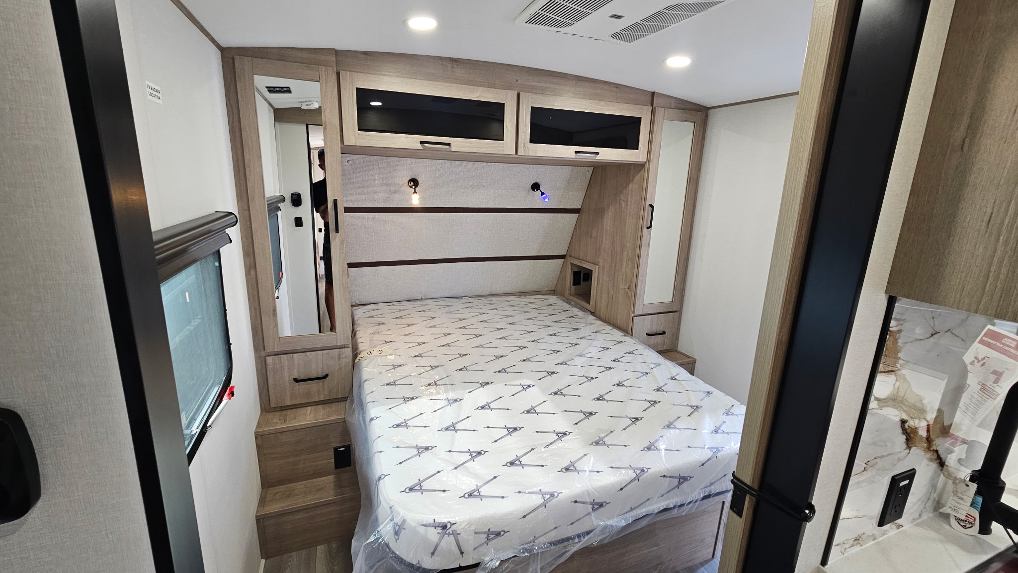 Explore this modern RV rental bedroom featuring a covered bed, ample storage, reading lights, and full-length mirrors.. Grand Design Imagine 2026
