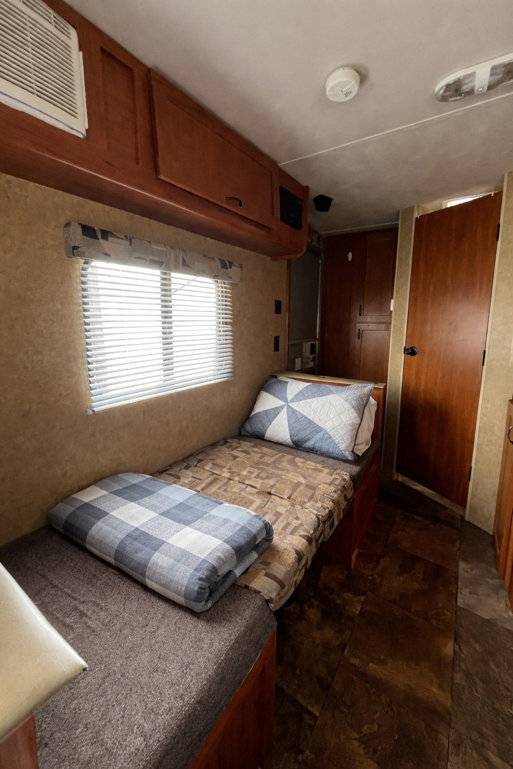 This RV rental offers a compact bedroom with two single beds, a window, and storage cabinets overhead. Ideal for travel accommodation.. Forest River Cherokee Wolf Pup 2014