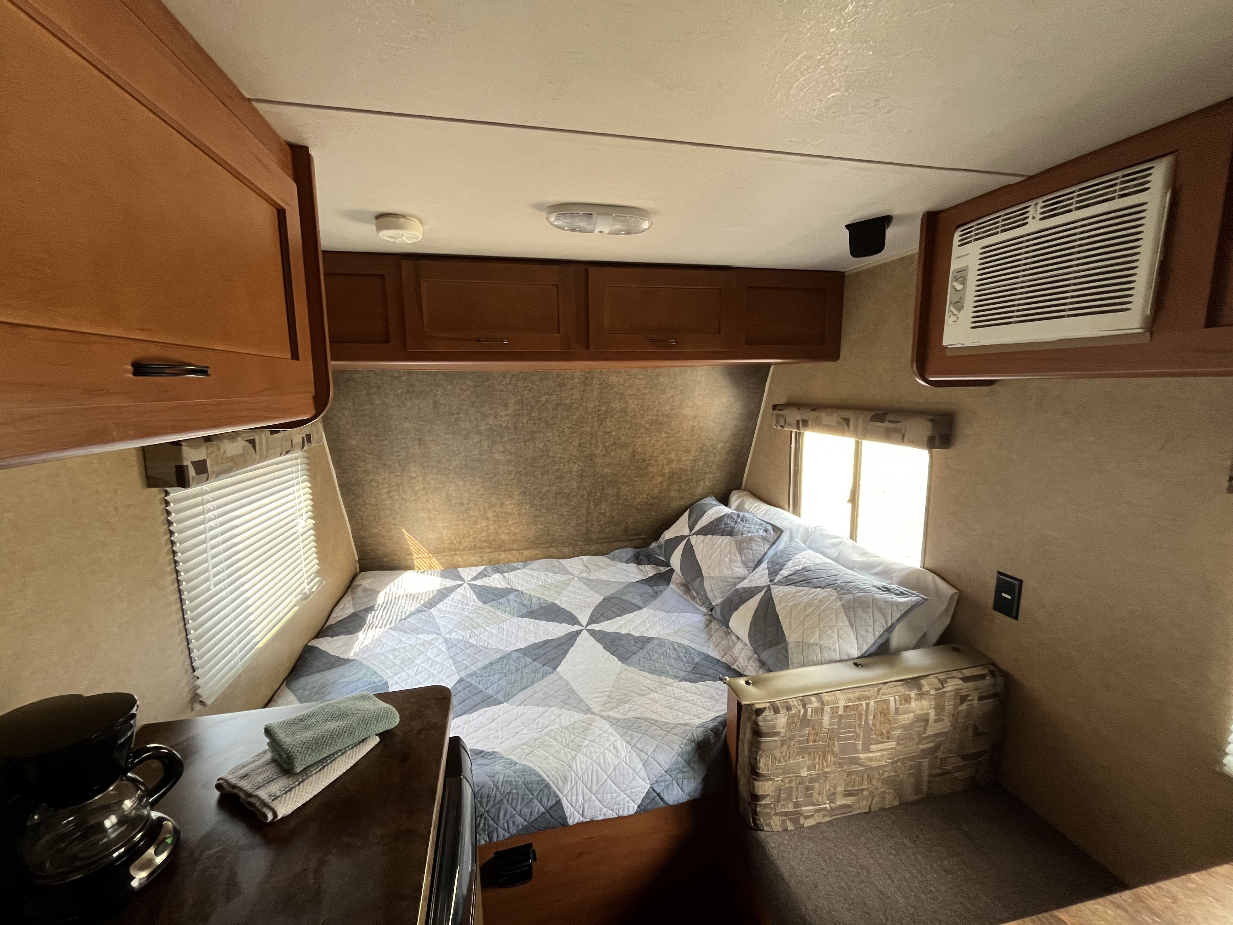 RV rental bedroom: a comfortable bed with a patterned quilt, sunlit windows, and convenient overhead storage.. Forest River Cherokee Wolf Pup 2014