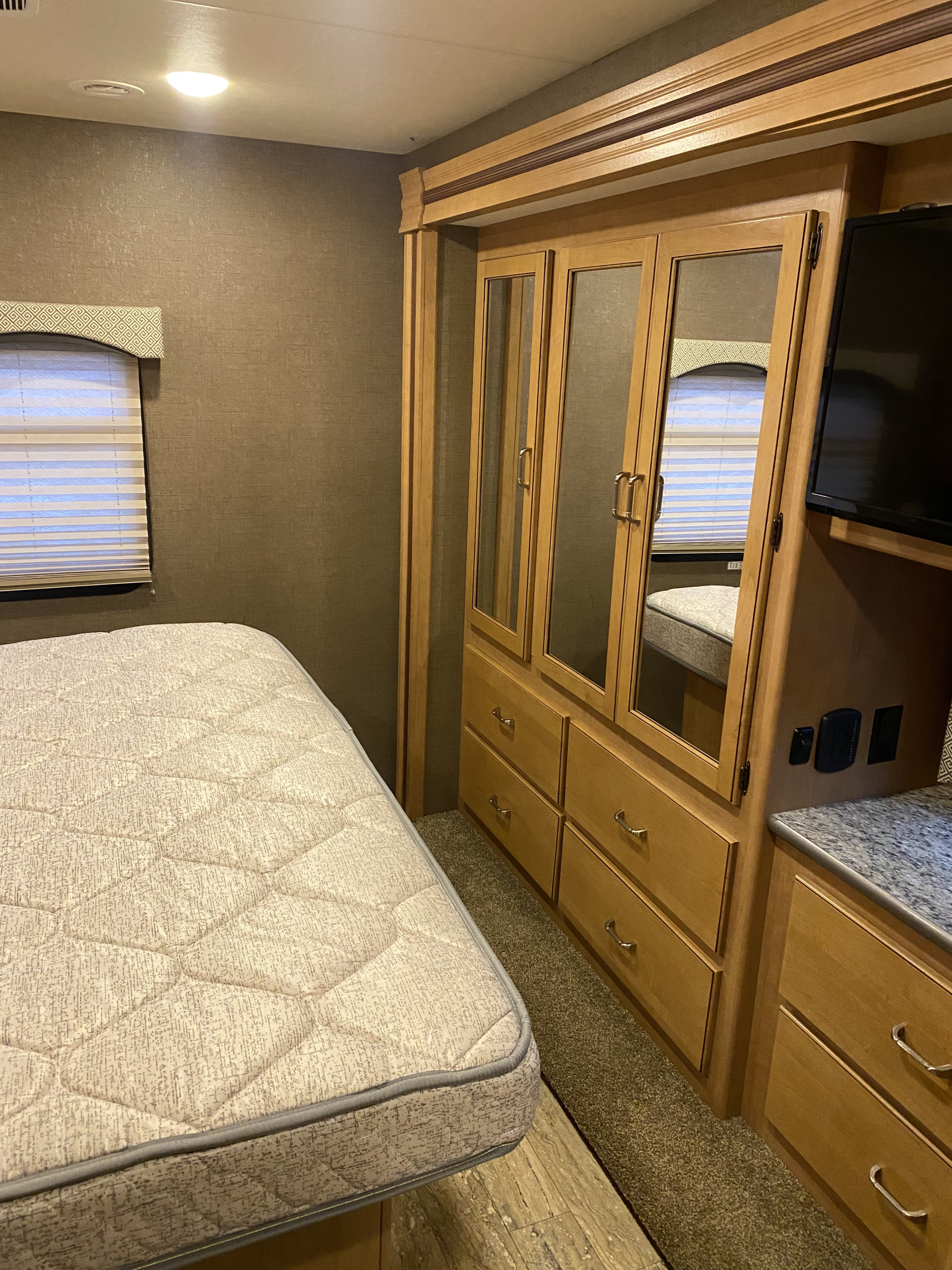 RV rental bedroom: comfortable bed, built-in mirrored wardrobe with drawers, window with blinds, and wall-mounted TV area.. Thor Hurricane 2017