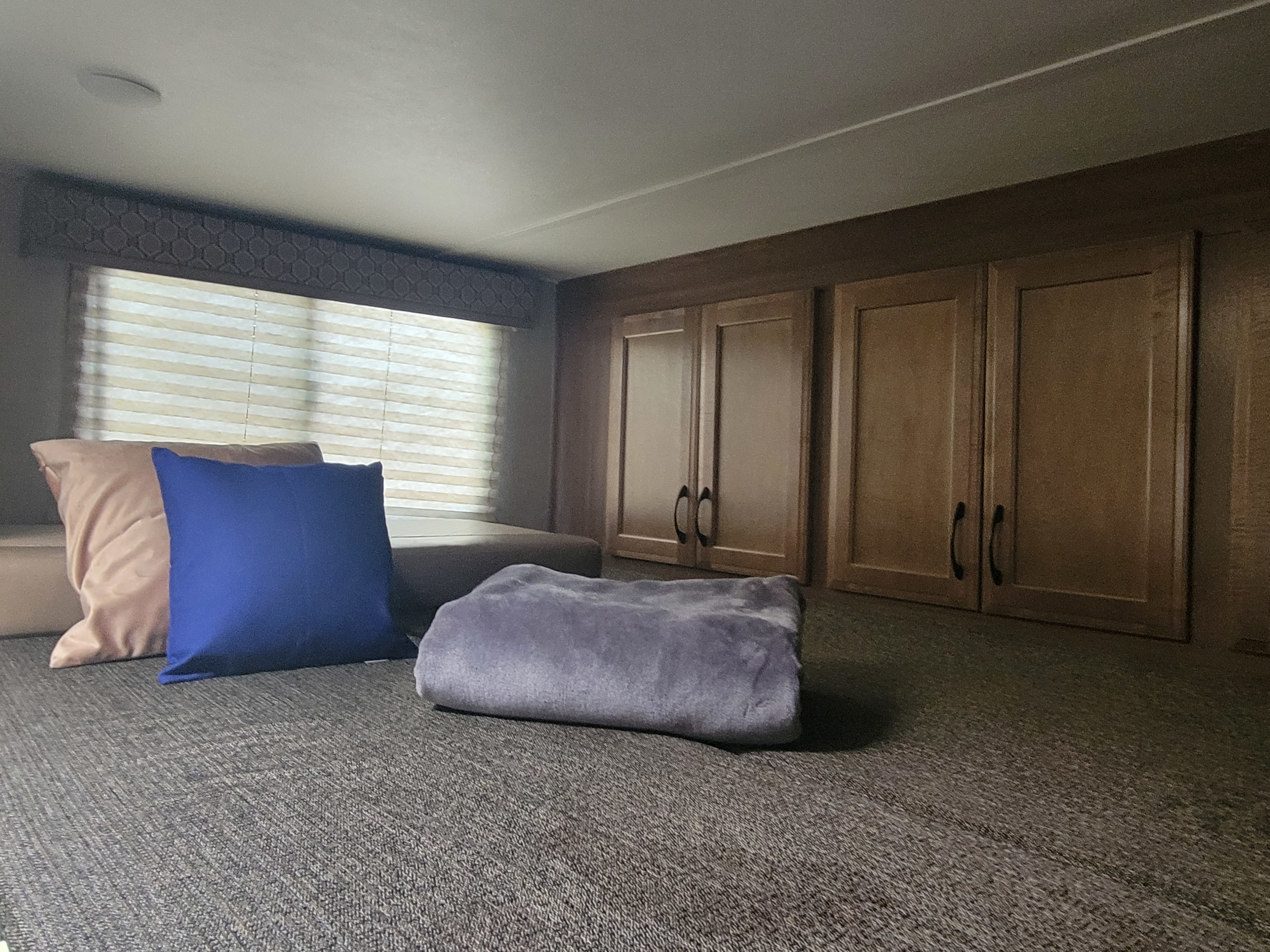 Cozy RV rental interior: a comfy bunk with pillows, a soft blanket, window blinds, and overhead storage cabinets.. Gulf Stream Conquest 2019