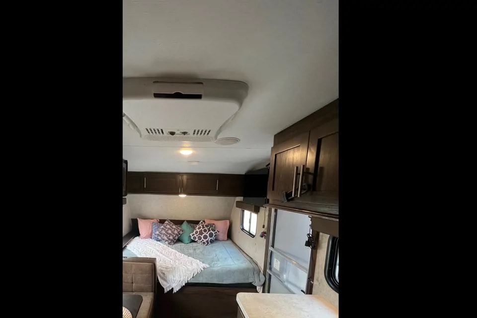 Cozy rv rental interior: view of the bed with colorful pillows, overhead cabinets, and a ceiling-mounted AC unit.. Forest River Cherokee Wolf Pup 2019