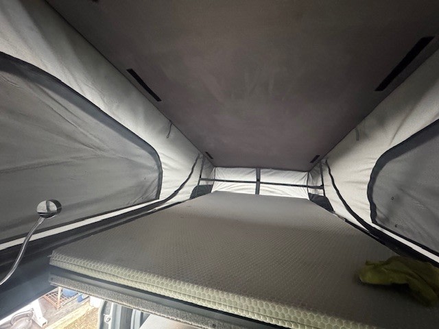 Inside this rv rental pop-top camper: a raised sleeping area with a textured mattress, light fabric walls, and mesh windows.. Mercedes-Benz Metris 2018