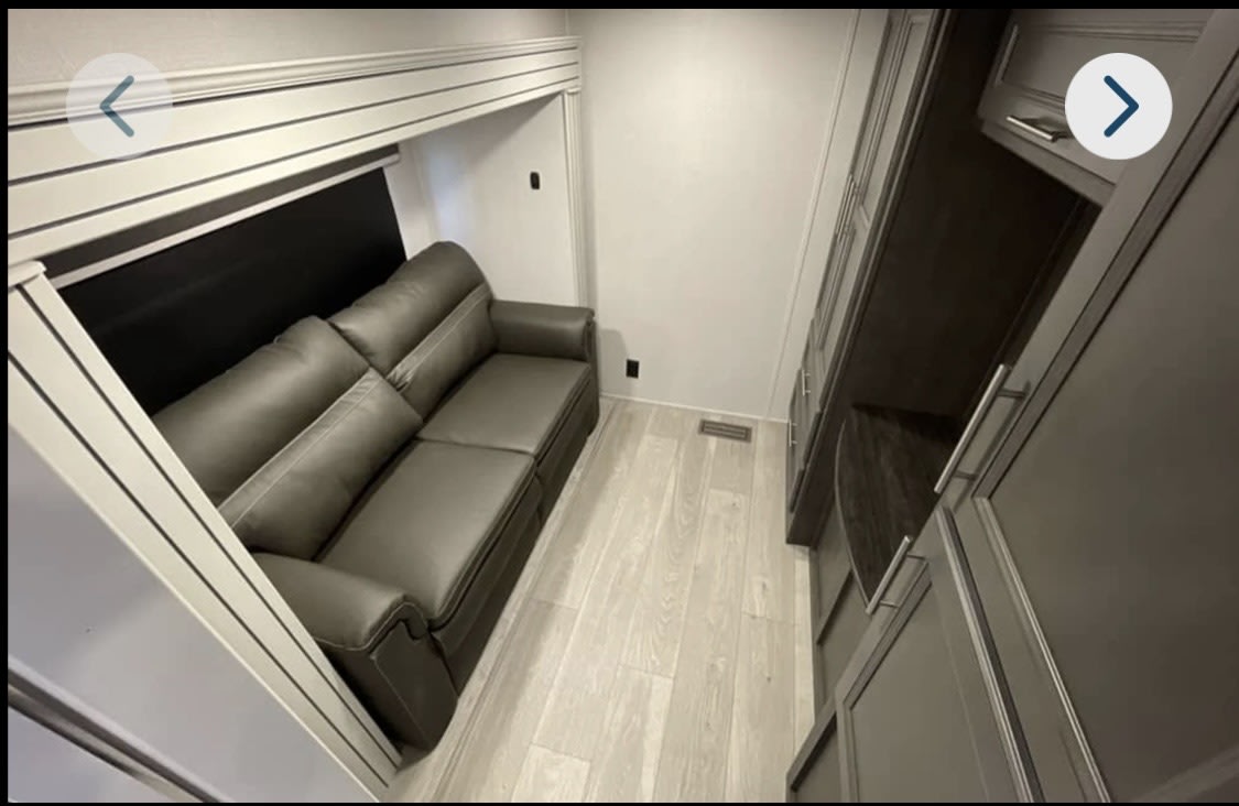 Cozy RV rental interior with a gray sofa in a slide-out, light wood flooring, and dark storage cabinets.. Keystone RV Cougar 2025