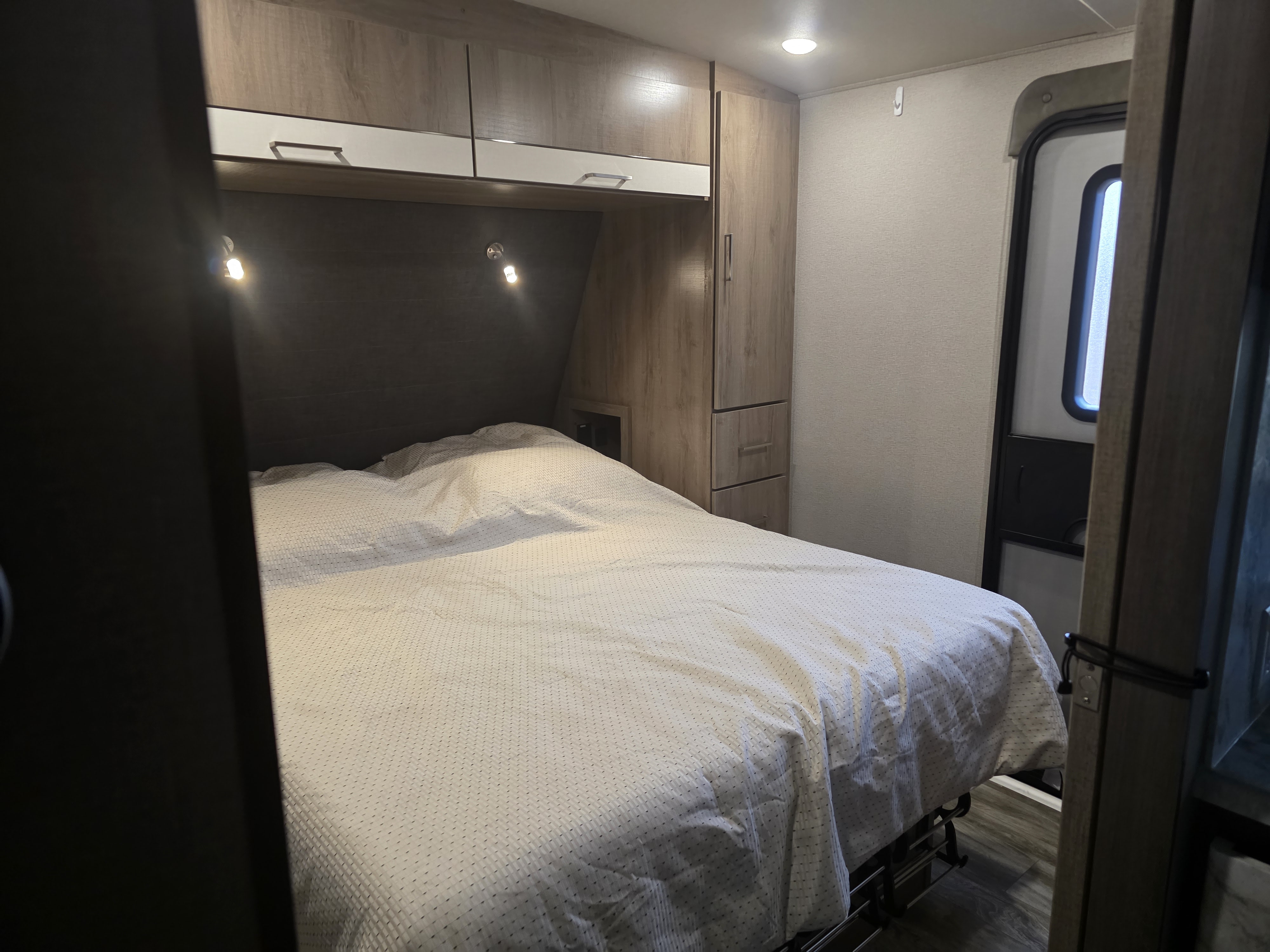 Inside an rv rental: a cozy bedroom with a neatly made bed, overhead cabinets, built-in wardrobe, and an exit door.. Grand Design Imagine 2022