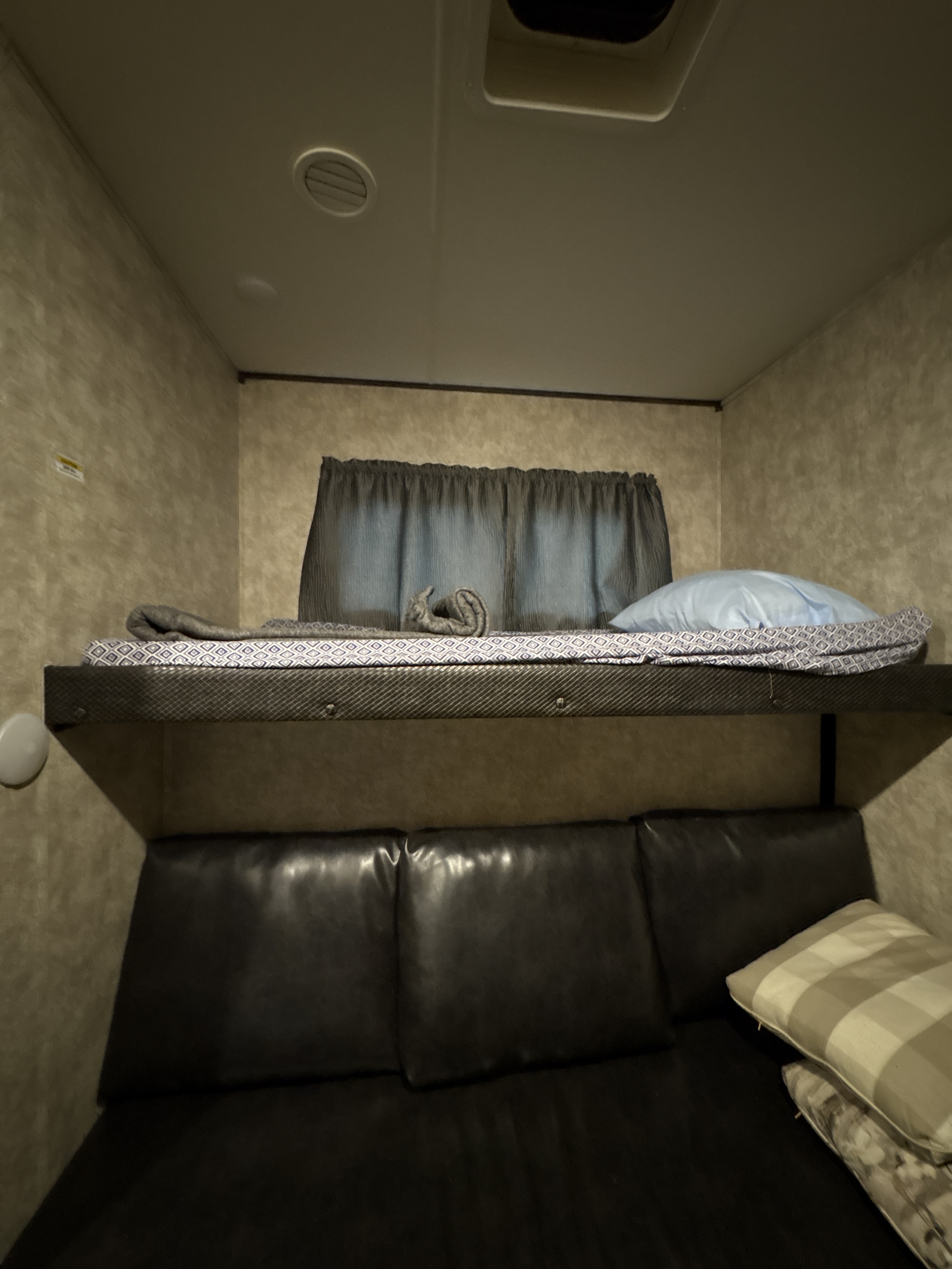 Inside this rv rental, a bunk bed with blue and patterned bedding sits above a dark leather-like sofa with striped pillows.. Mesa Ridge 384bhs 2018