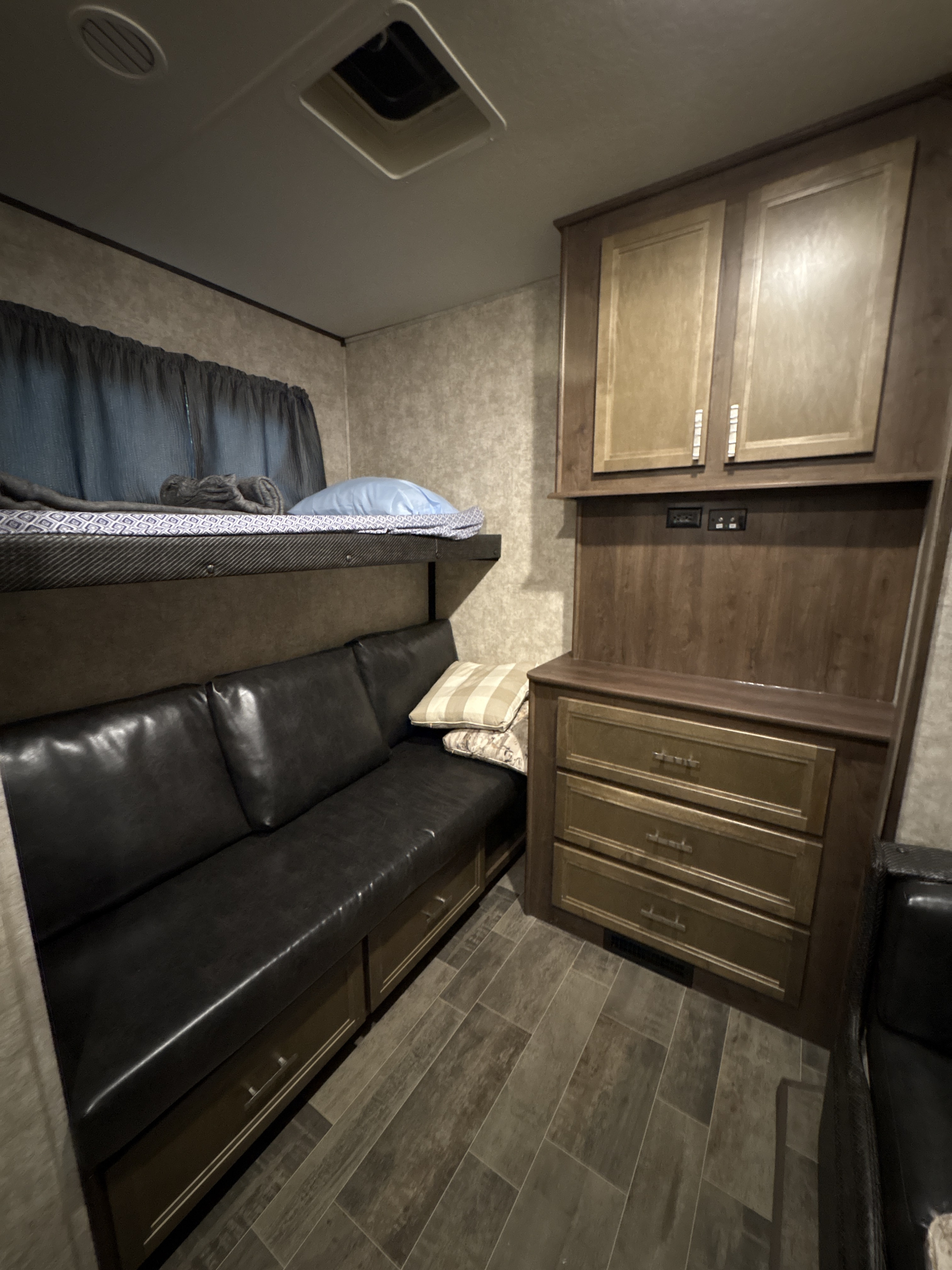 This cozy rv rental interior features a bunk bed, black sofa with under-seat storage, and wood-look cabinets.. Mesa Ridge 384bhs 2018