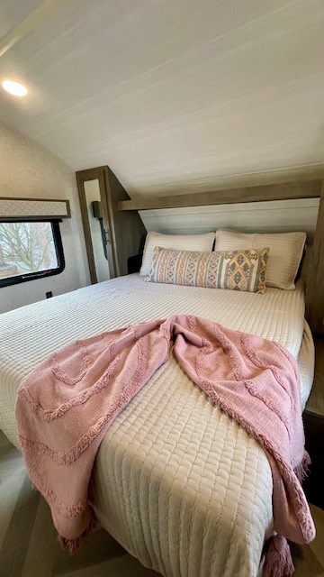 Stylish RV rental bedroom features a quilted bed, soft pink throw, and decorative pillows under an angled ceiling.. Forest River Salem Cruise Lite 2021
