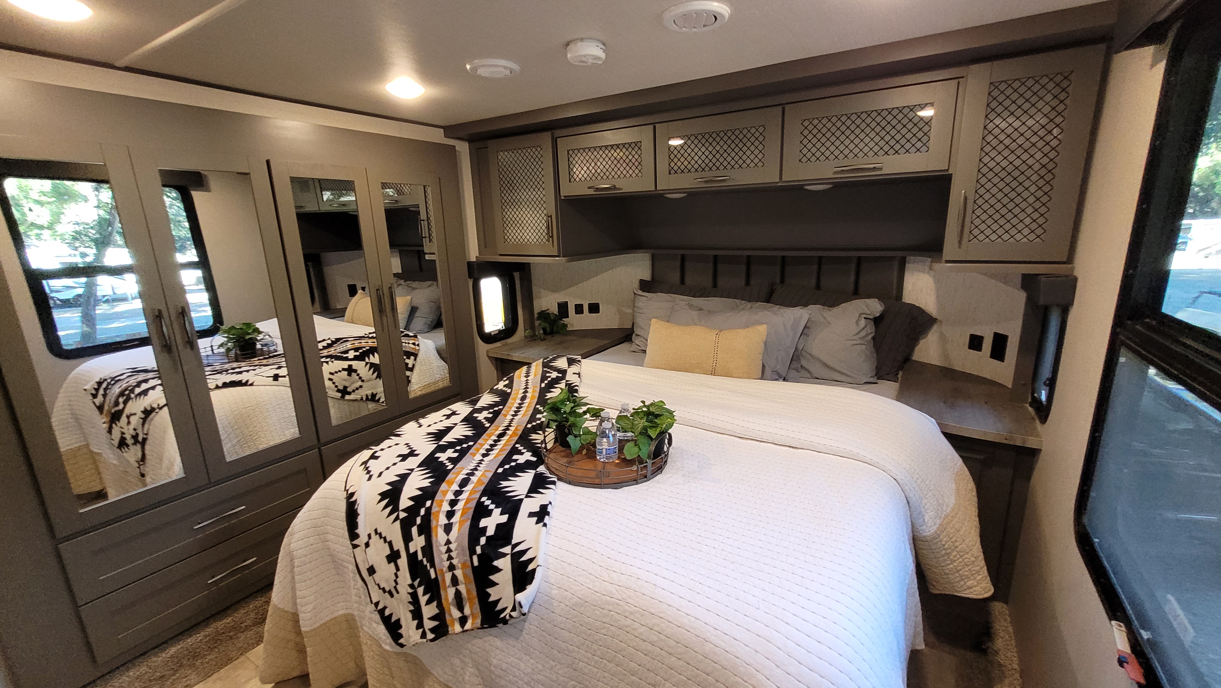 Inviting RV rental bedroom with a comfy bed, stylish throw, ample storage, and bright windows for your next trip.. Grand Design Momentum Toy Hauler 2021