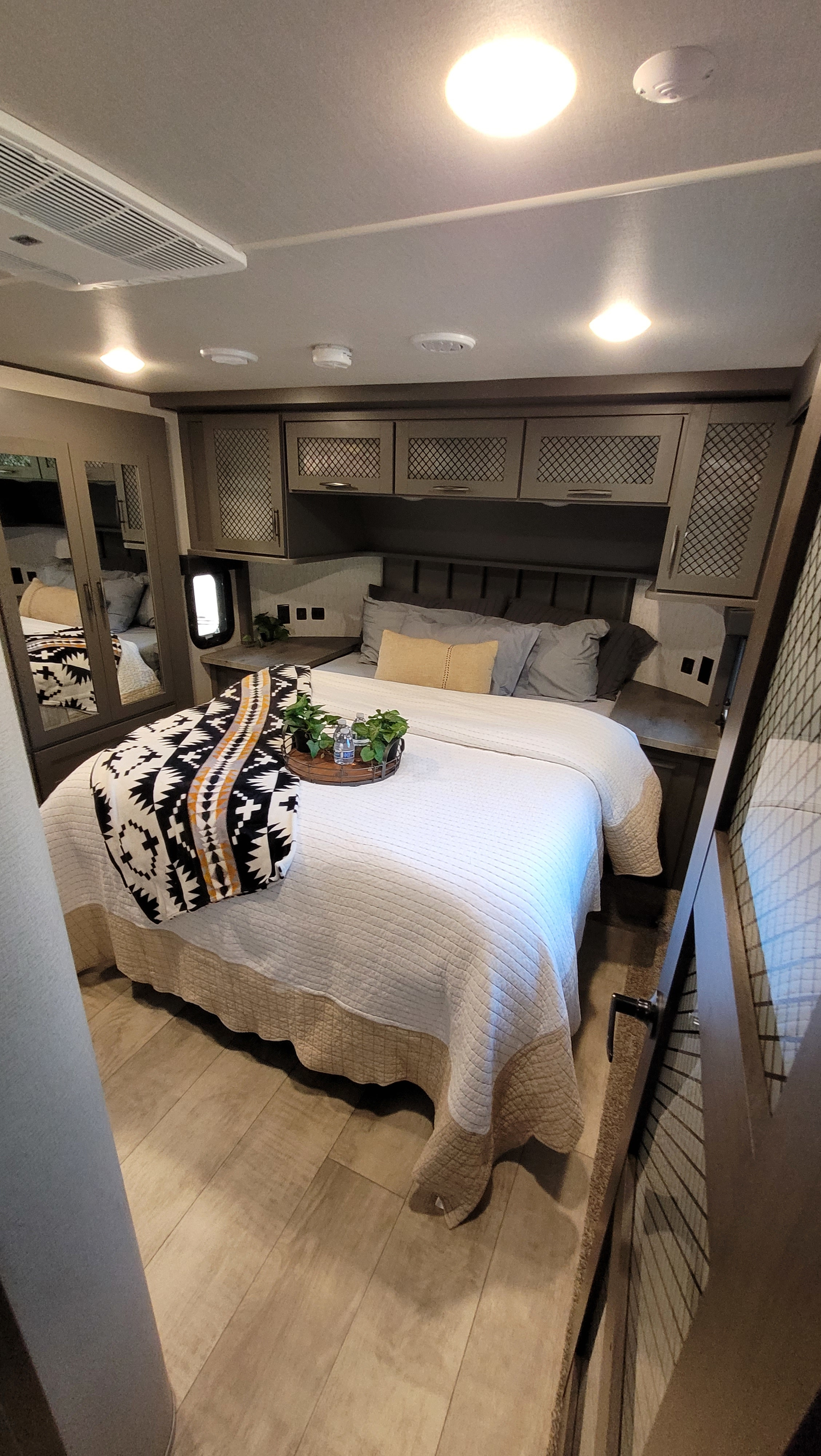 RV rental: A cozy bedroom with a large bed, stylish overhead cabinets, mirrored closet, and wood-look floor.. Grand Design Momentum Toy Hauler 2021