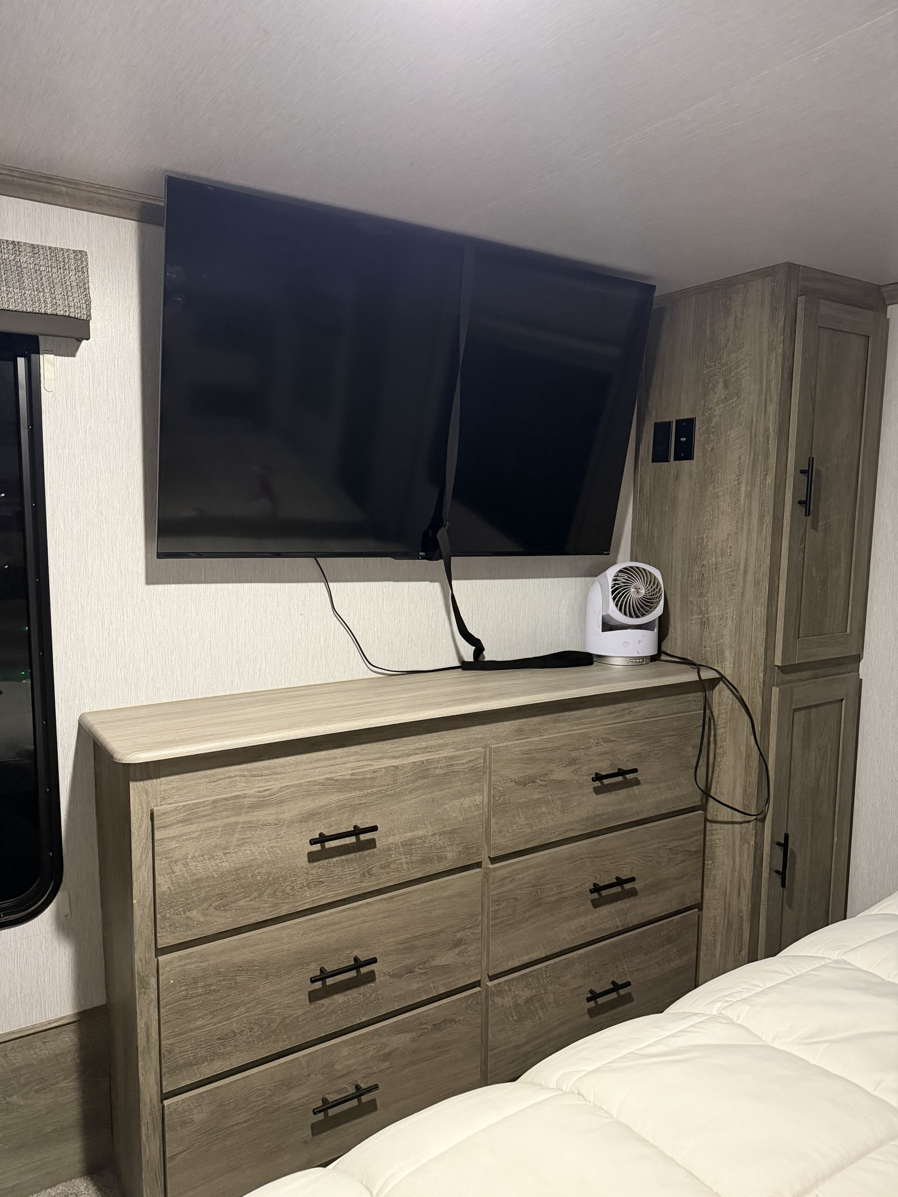 RV rental bedroom showing a wall-mounted TV over a wooden dresser, storage cabinet, and bed with white comforter.. Forest River Salem Hemisphere 2022