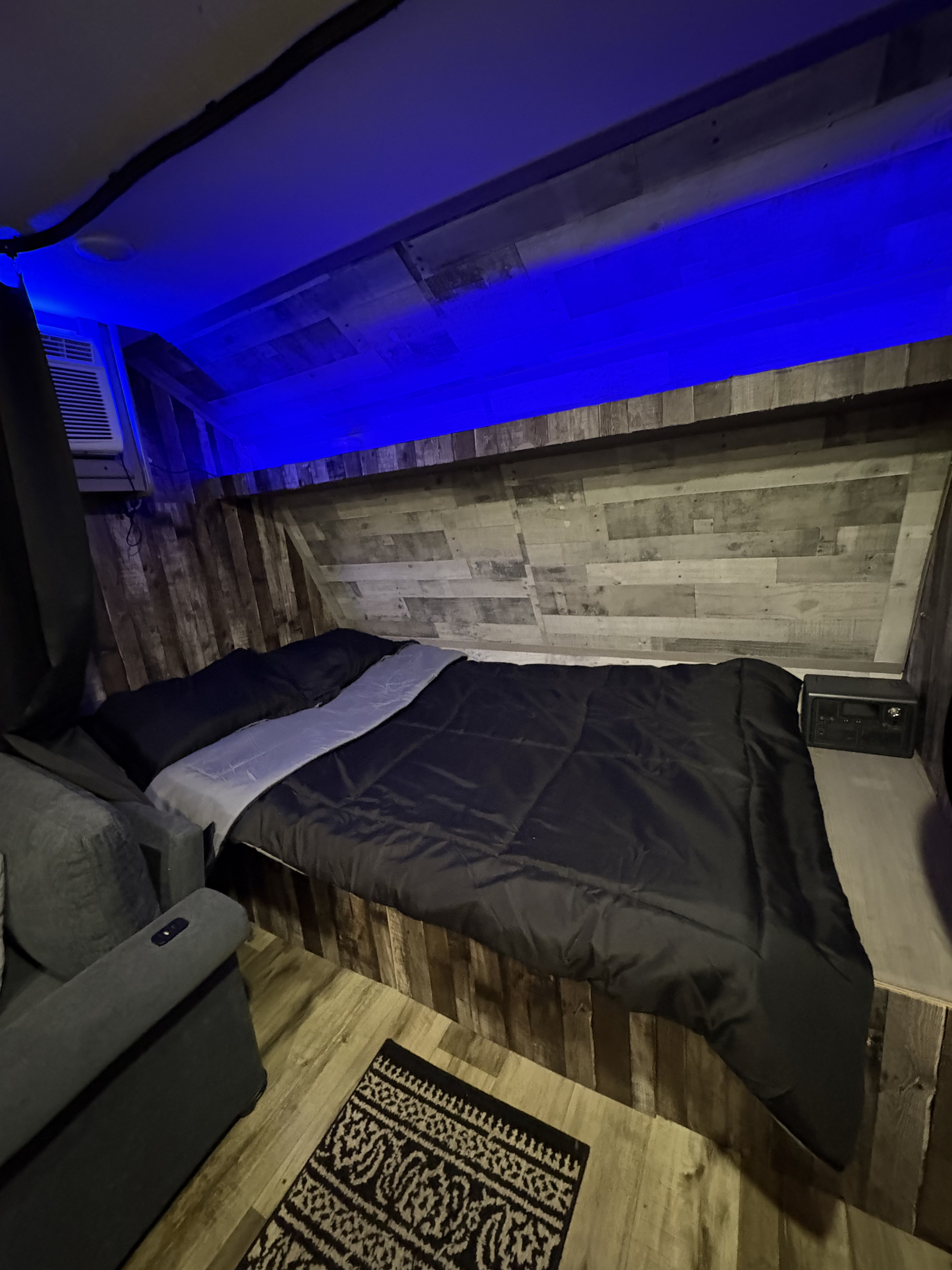 RV rental bedroom featuring a cozy bed, armchair, AC, blue LED lighting, and rustic wood walls, perfect for a compact stay.. Dutchmen Coleman Lantern LT 2023
