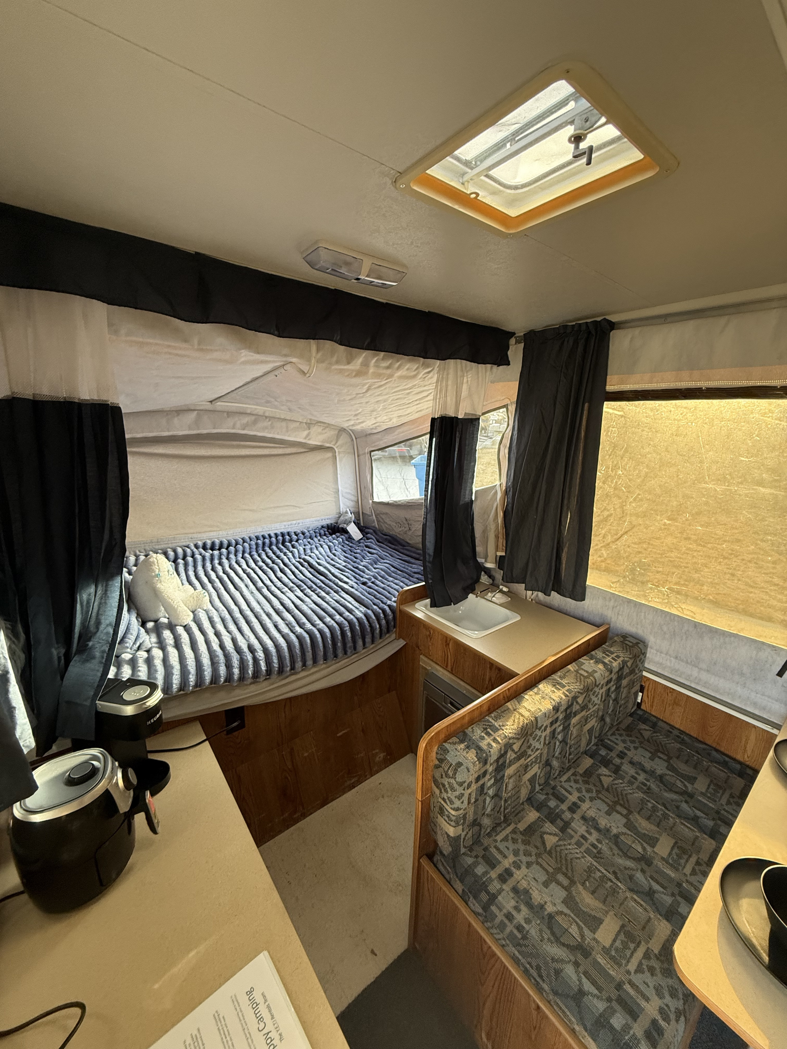Inside this RV rental pop-up camper: a bed with a plush blanket, compact kitchen, and dinette for camping comfort.. Dutchmen Voyager 2000