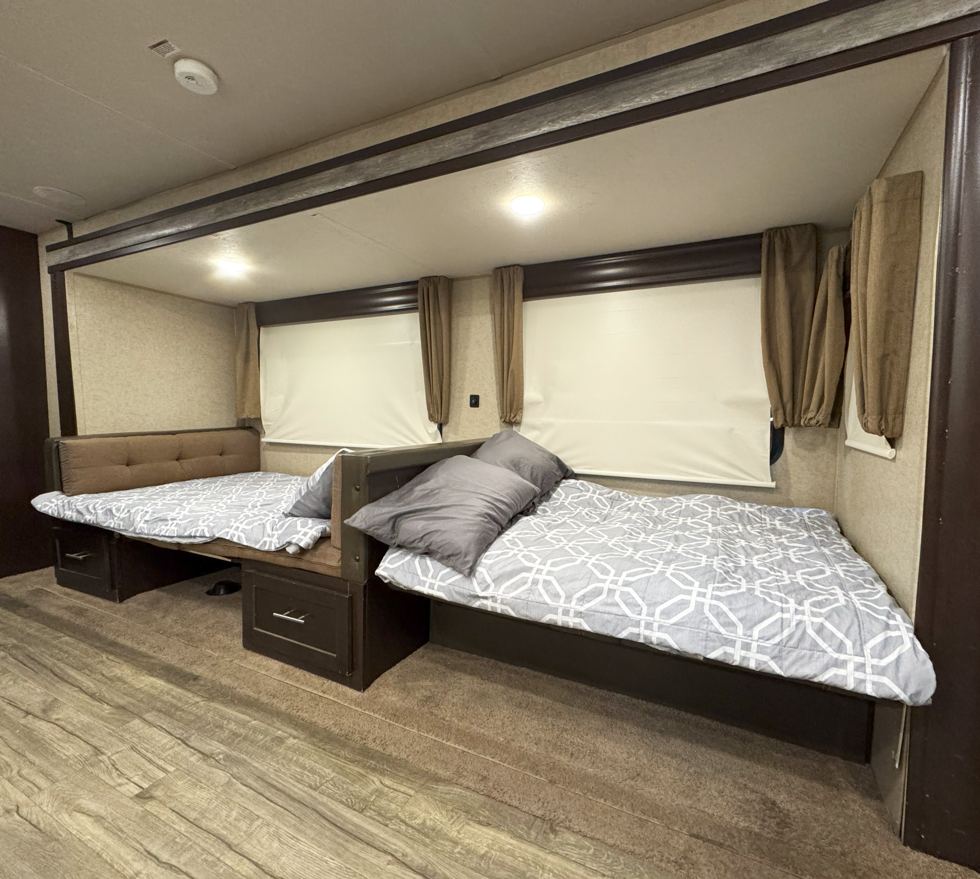 RV rental interior: two comfortable beds with grey bedding, pillows, and under-bed storage. Windows have blinds & curtains.. Forest River Cherokee 2017
