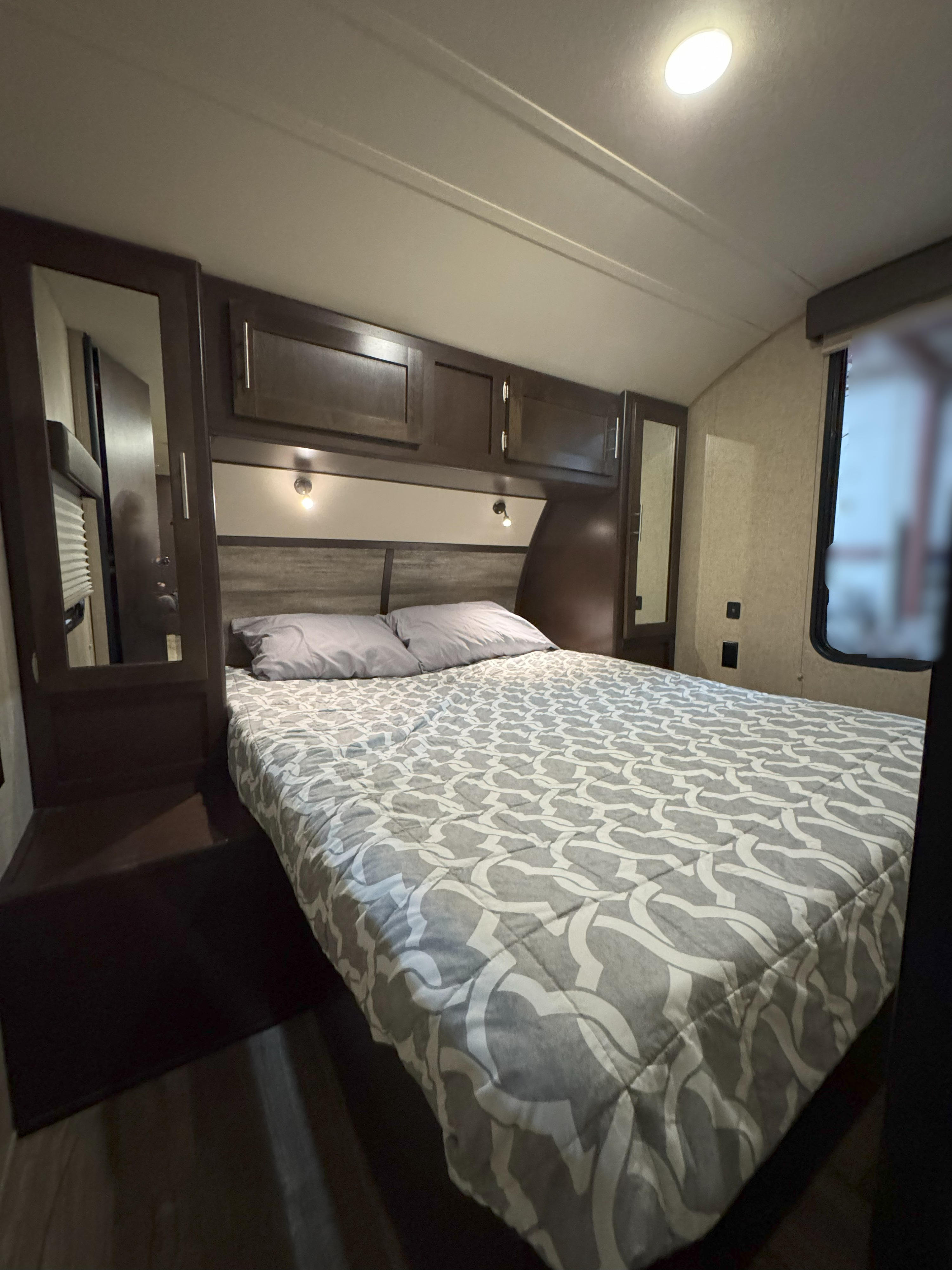 Cozy RV rental bedroom featuring a comfortable bed with patterned comforter, overhead storage, and reading lights.. Forest River Cherokee 2017