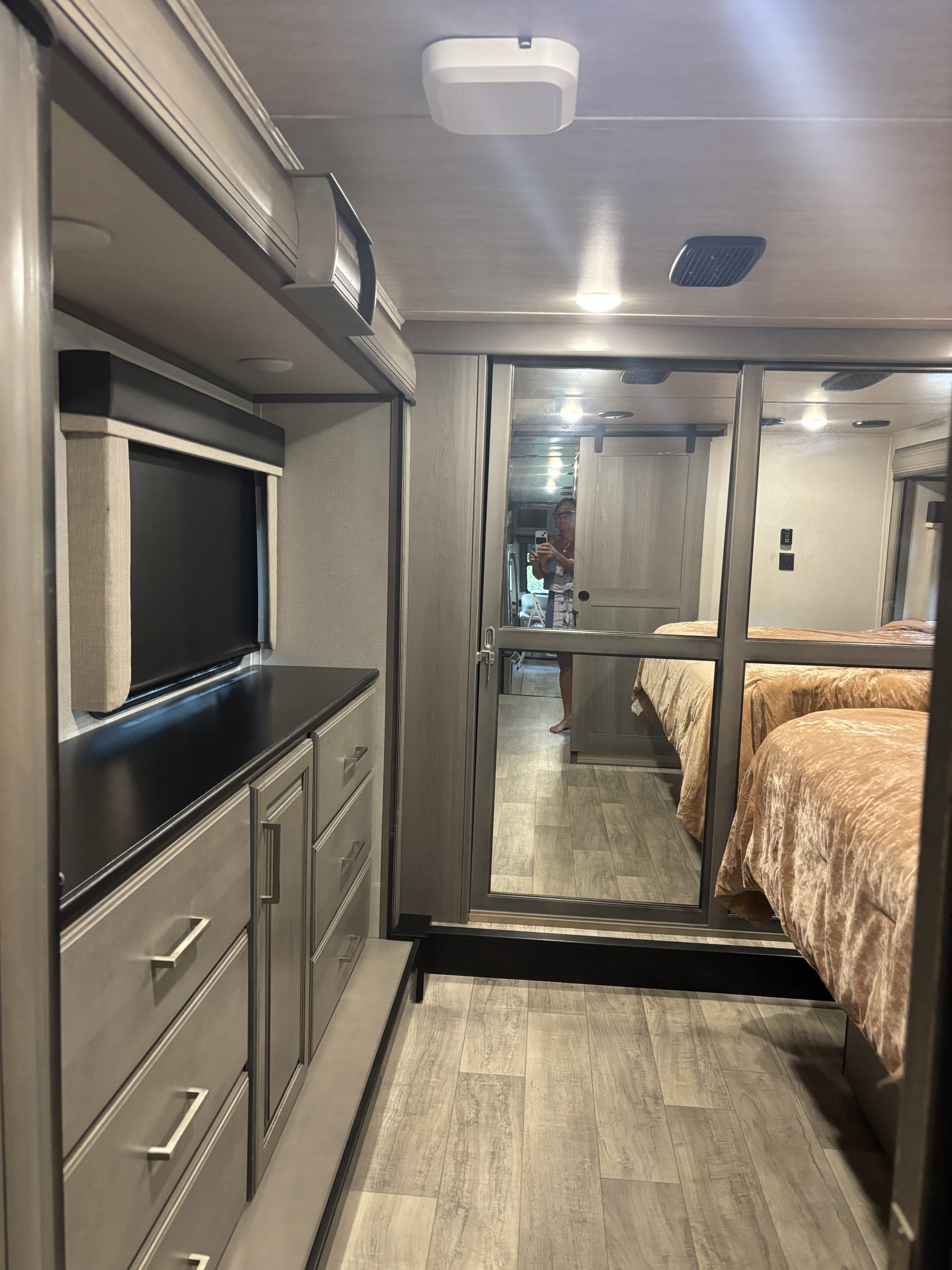 Modern RV rental bedroom area with mirrored closet doors reflecting a bed, a built-in dresser, and light wood flooring.. Keystone RV Montana 2021