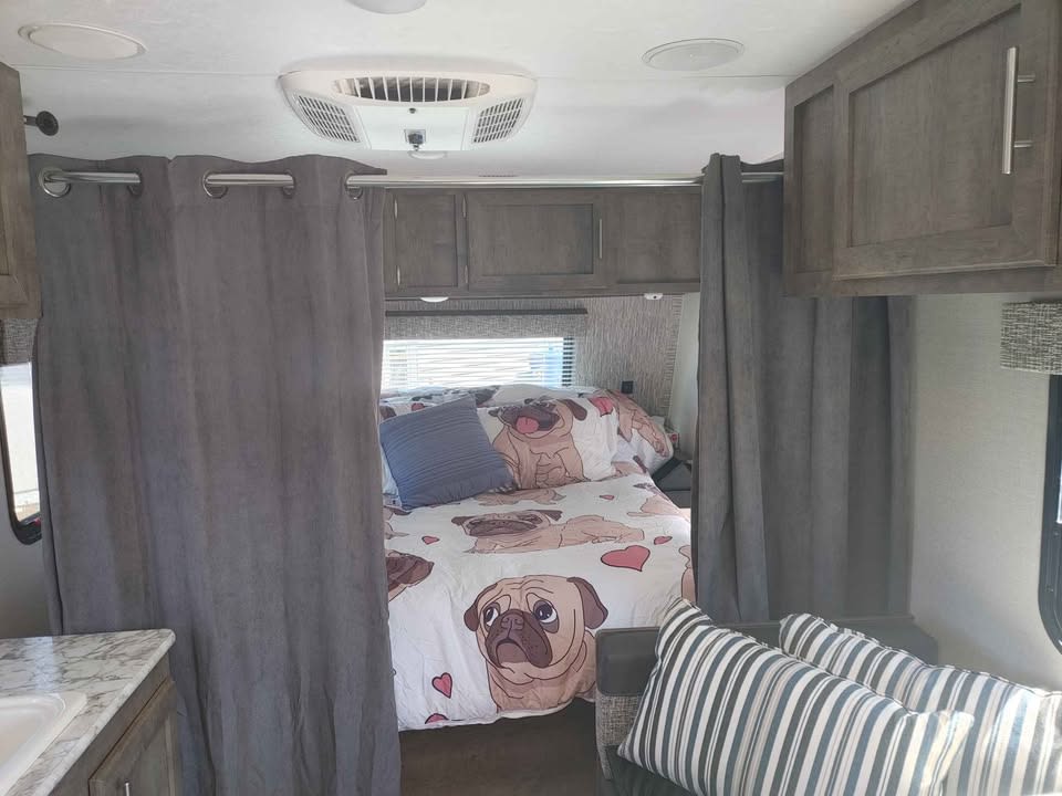 This RV rental features a cozy bedroom with pug-themed bedding, privacy curtains, and a small sitting area.. KZ Sportmen classic 160 QB 2019