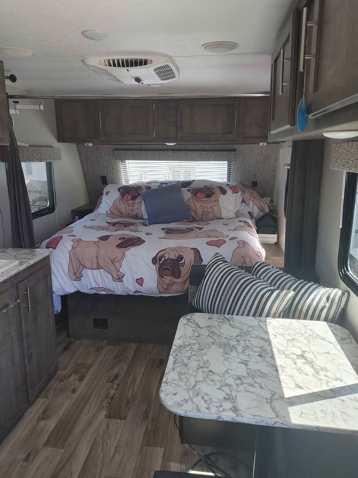 This cozy RV rental features a bright bedroom with pug-themed bedding, overhead cabinets, wood-look floors, and a marbled dining table.. KZ Sportmen classic 160 QB 2019
