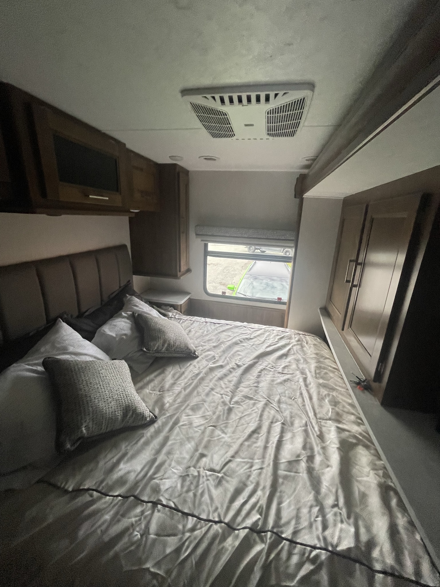 Cozy RV rental bedroom featuring a neatly made bed, padded headboard, window with a view, and overhead AC unit.. Coachmen Mirada 2021