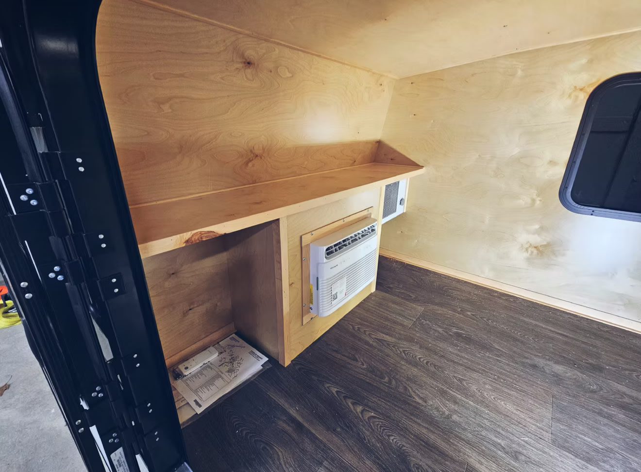 Step inside this cozy RV rental with natural wood walls, dark flooring, integrated AC unit, and built-in storage shelving.. Adventurer 5x8 Utility Camper Trailer 2025