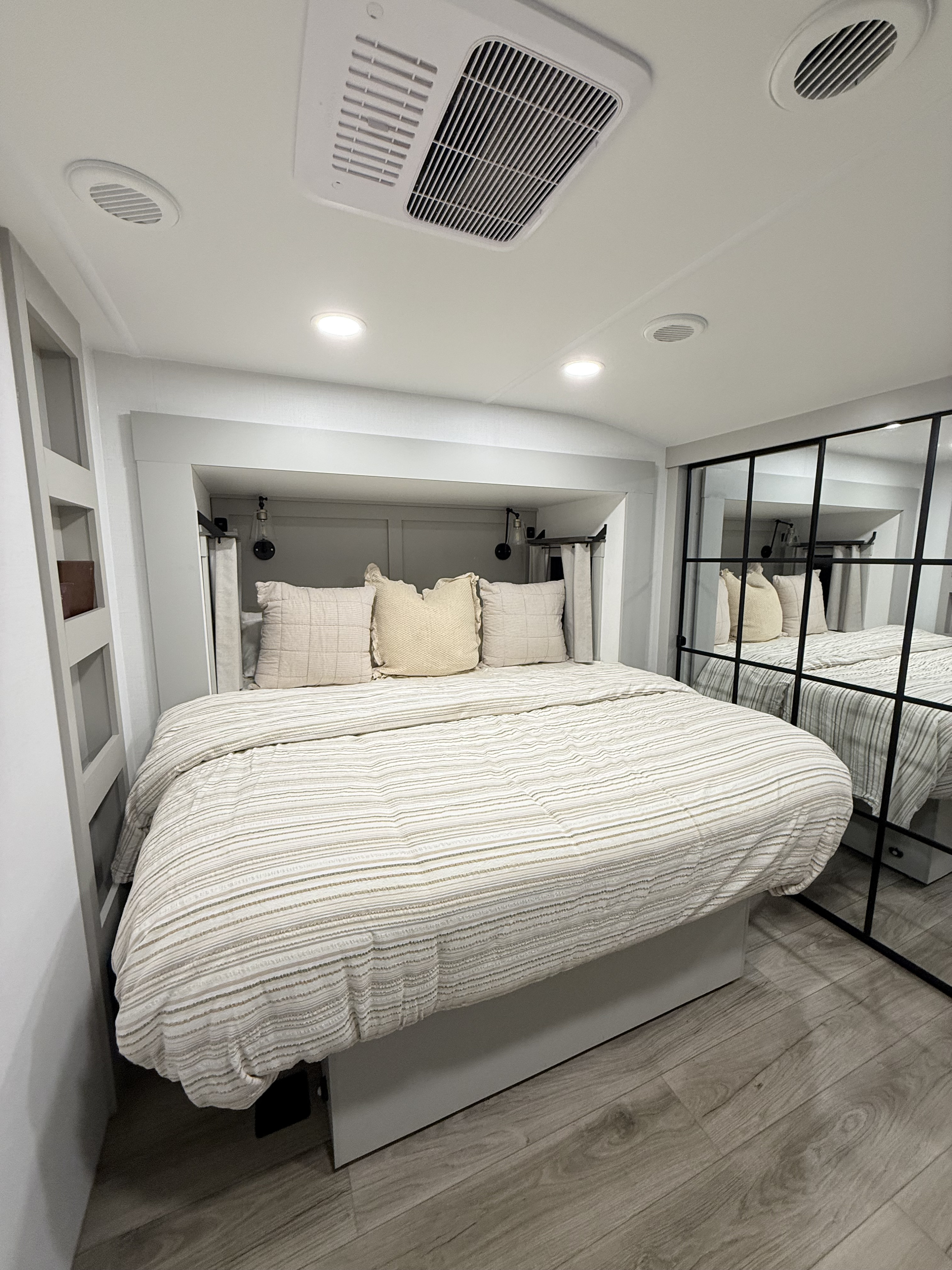 Experience comfort in this modern RV rental bedroom, featuring a striped bed, mirrored wardrobe, and overhead AC.. Brinkley RV Model Z 2025
