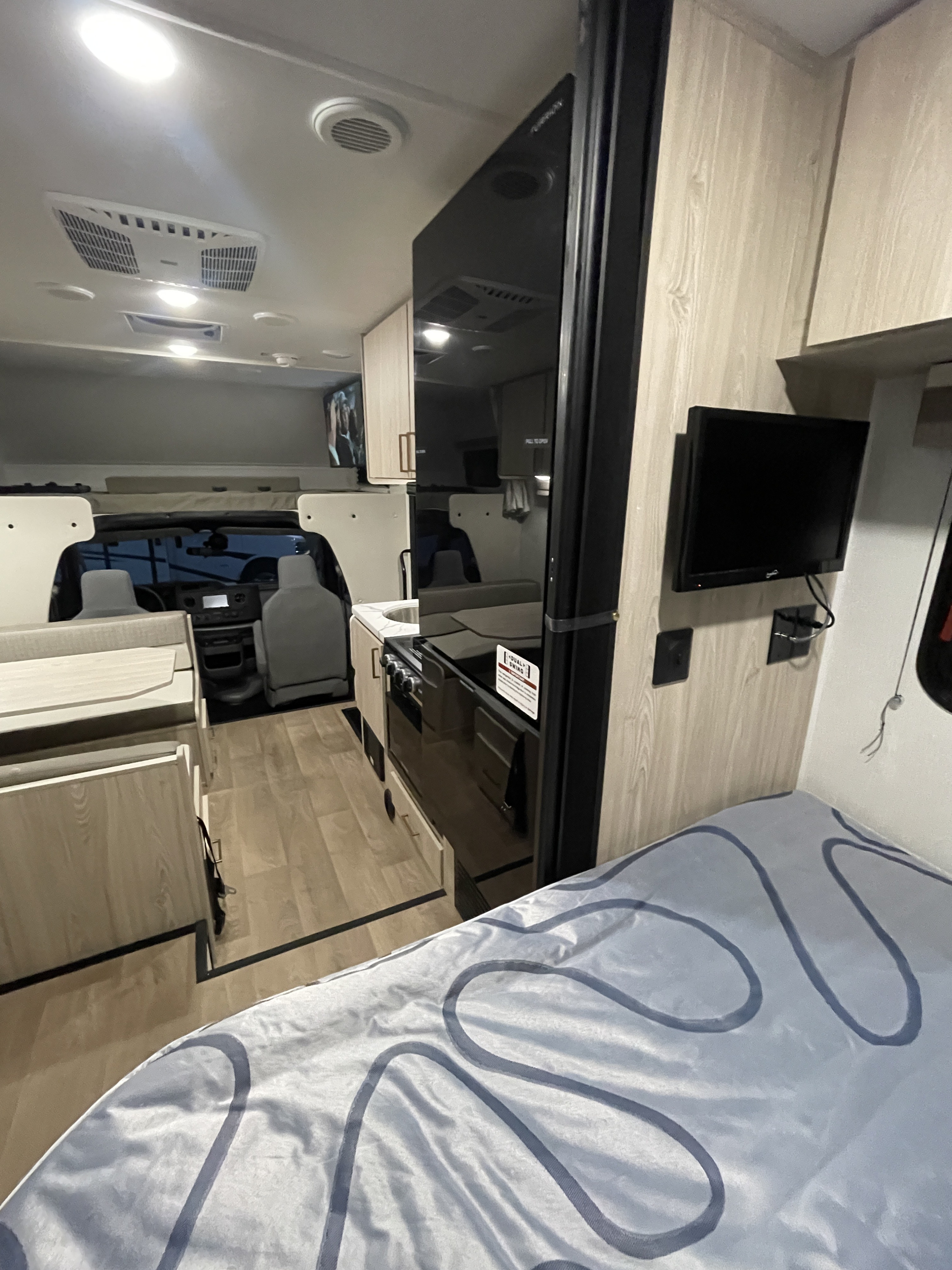 Inside an rv rental: foreground bed, mid-ground kitchenette, dinette, and driver's cabin visible in this compact living area.. Coachmen Leprechaun 2026