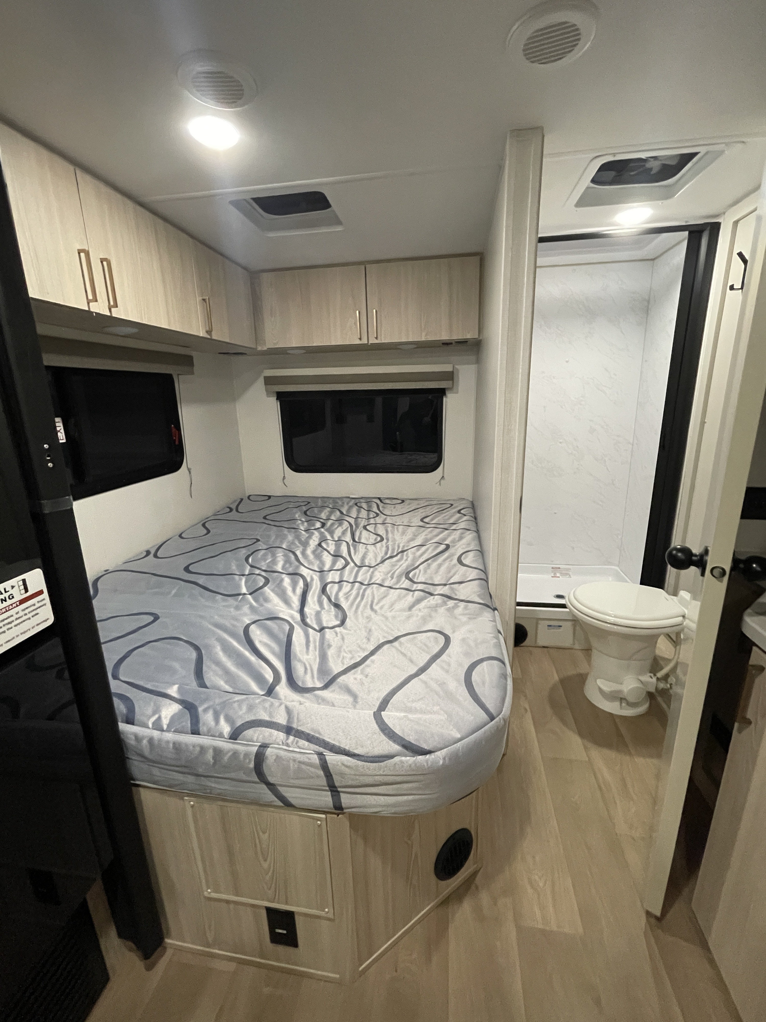 Compact RV rental interior featuring a bed, overhead cabinets, and a small bathroom with toilet and shower.. Coachmen Leprechaun 2026