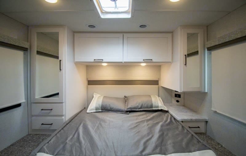 Compact RV rental bedroom interior with a cozy bed, overhead storage, mirrored cabinets, and bedside drawers.. Thor four winds 2026